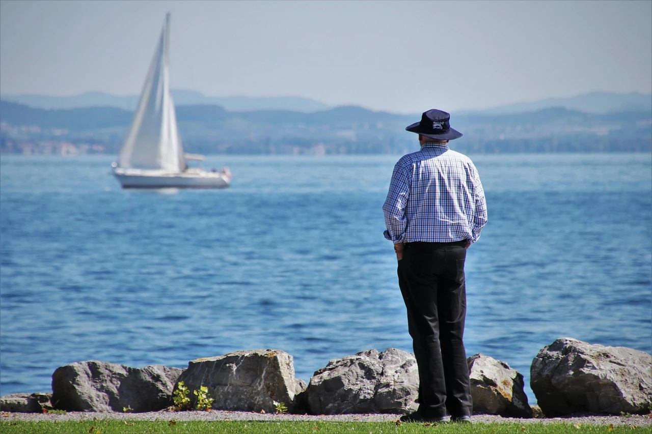 Mann mit Hut schaut auf ein Segelboot, das auf dem Bodensee fährt