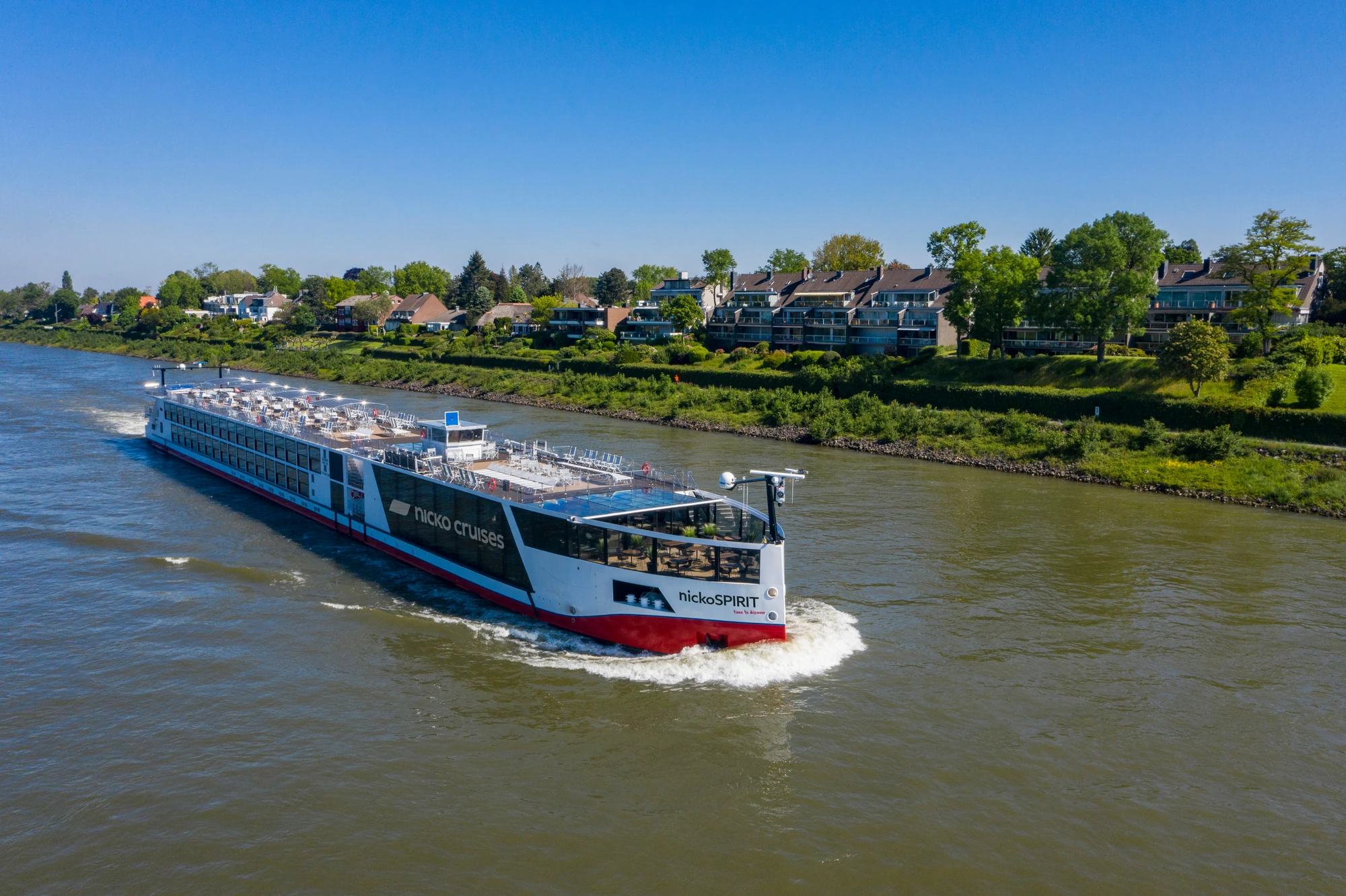 Blick auf die Außenansicht der nickoSPIRIT bei Fahrt auf einem Fluss an Hügeln und Häusern vorbei