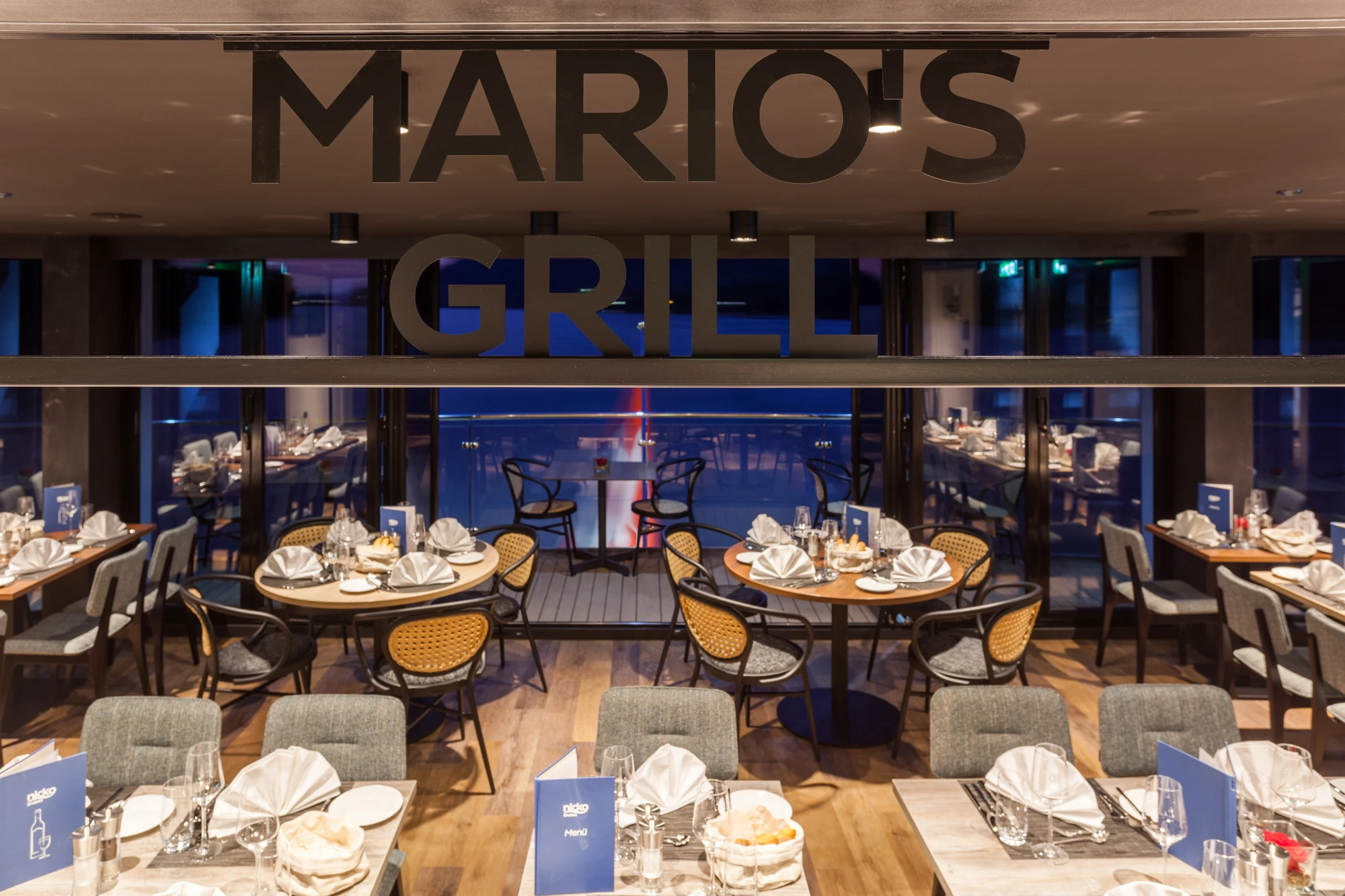 Schriftzug Mario's Grill mit gedeckten Tischen im Hintergrund am Abend