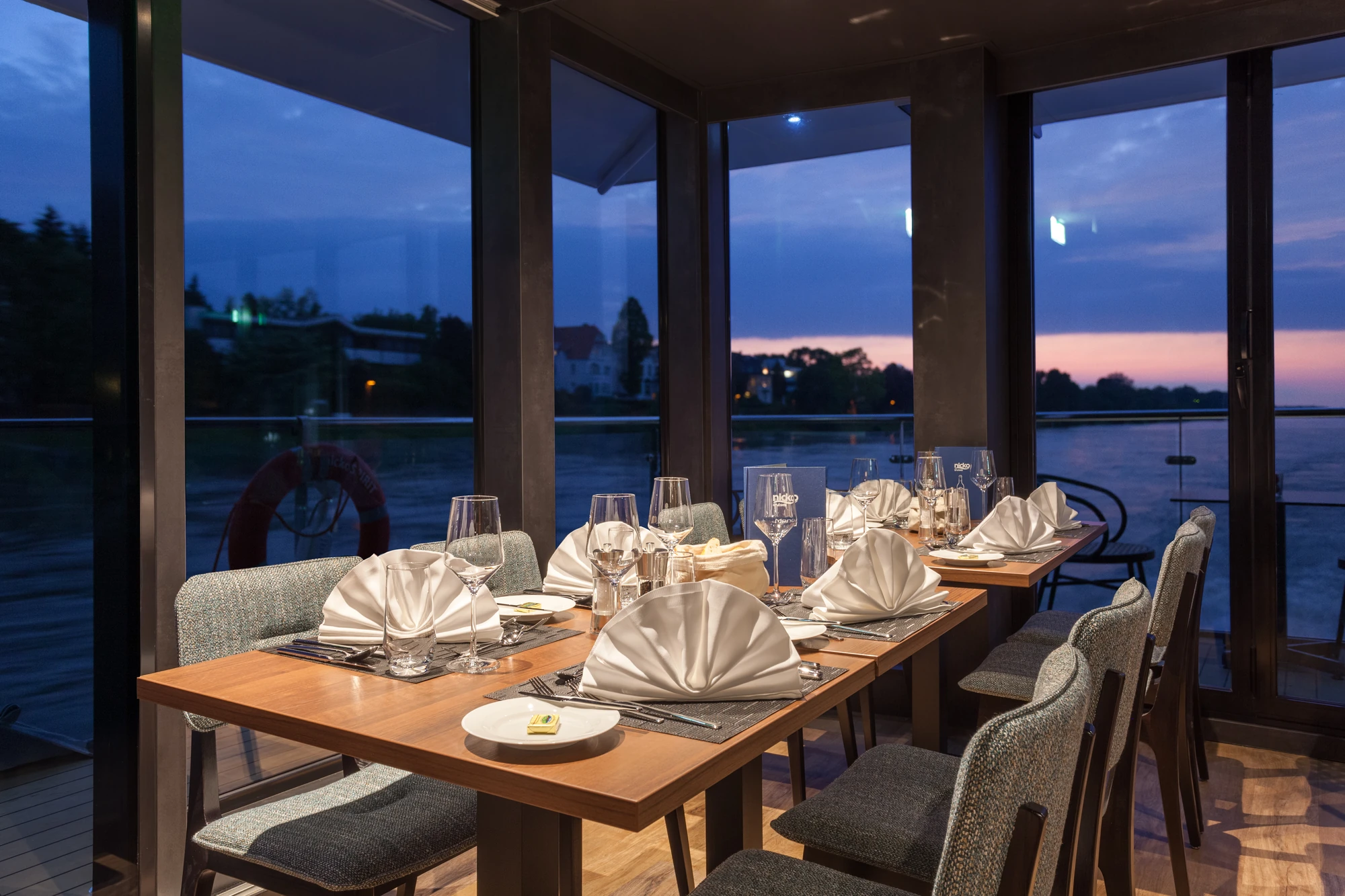 Gedeckter Tisch vor großen Panoramafenstern am Abend im Restaurant Marios Grill mit dunklem Himmel im Hintergrund