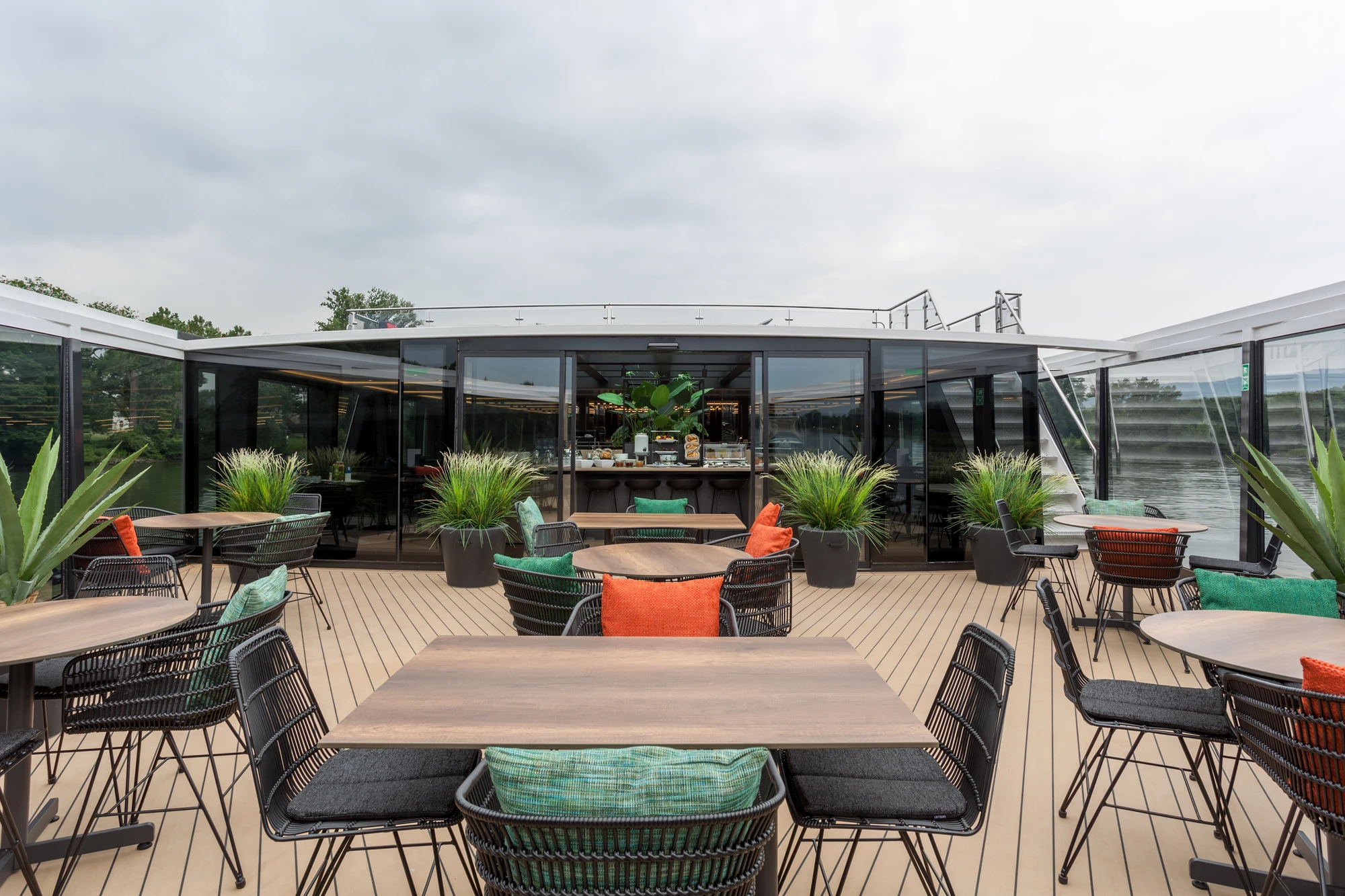 Tische und Stühle an Deck unter freiem Himmel mit bunten Sitzkissen und Pflanzen im Restaurant The Garden