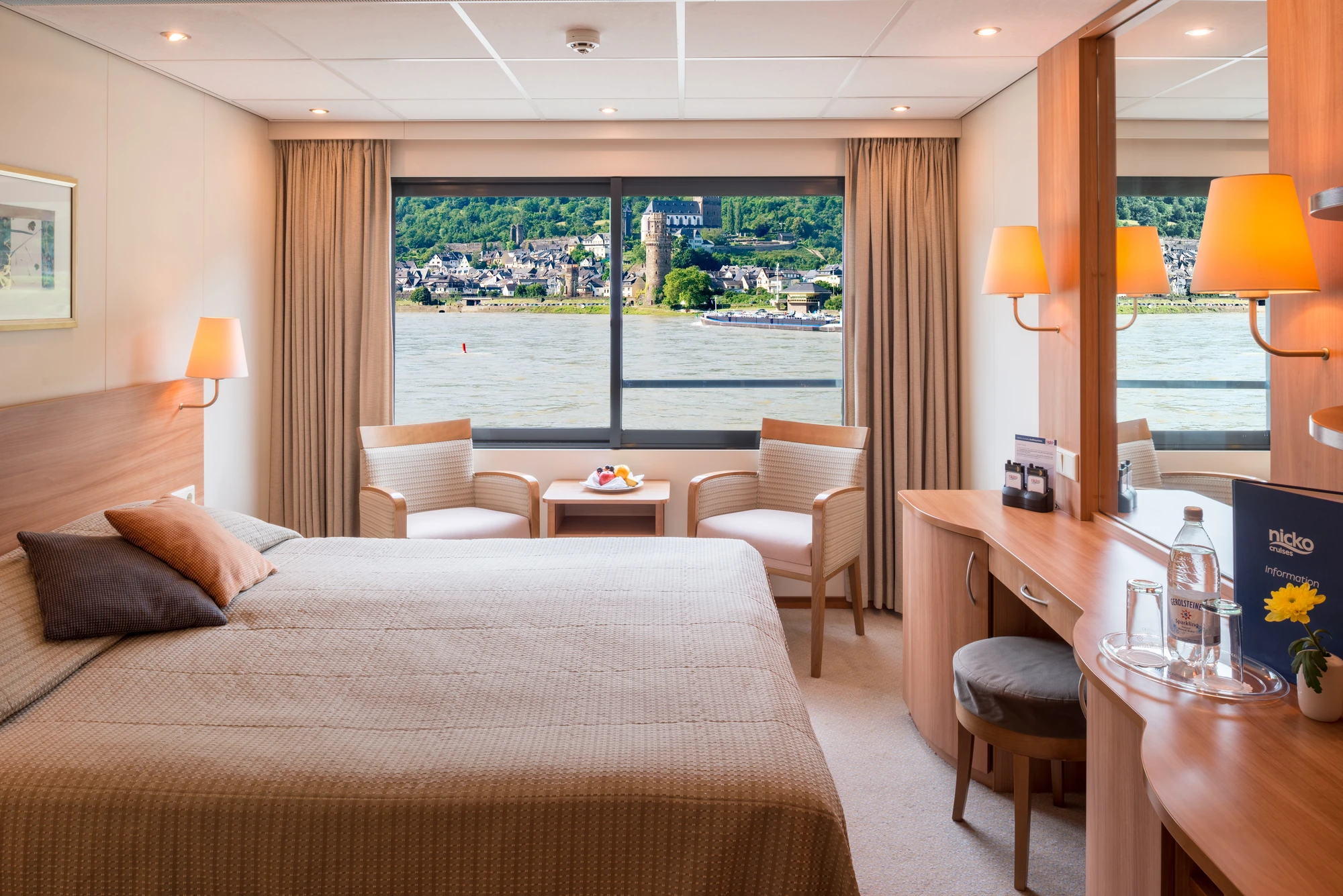 Kabine auf dem Mitteldeck mit einem Doppelbett und Sitzgelegenheit vor einem Panoramafenster und einem Tisch mit Spiegel