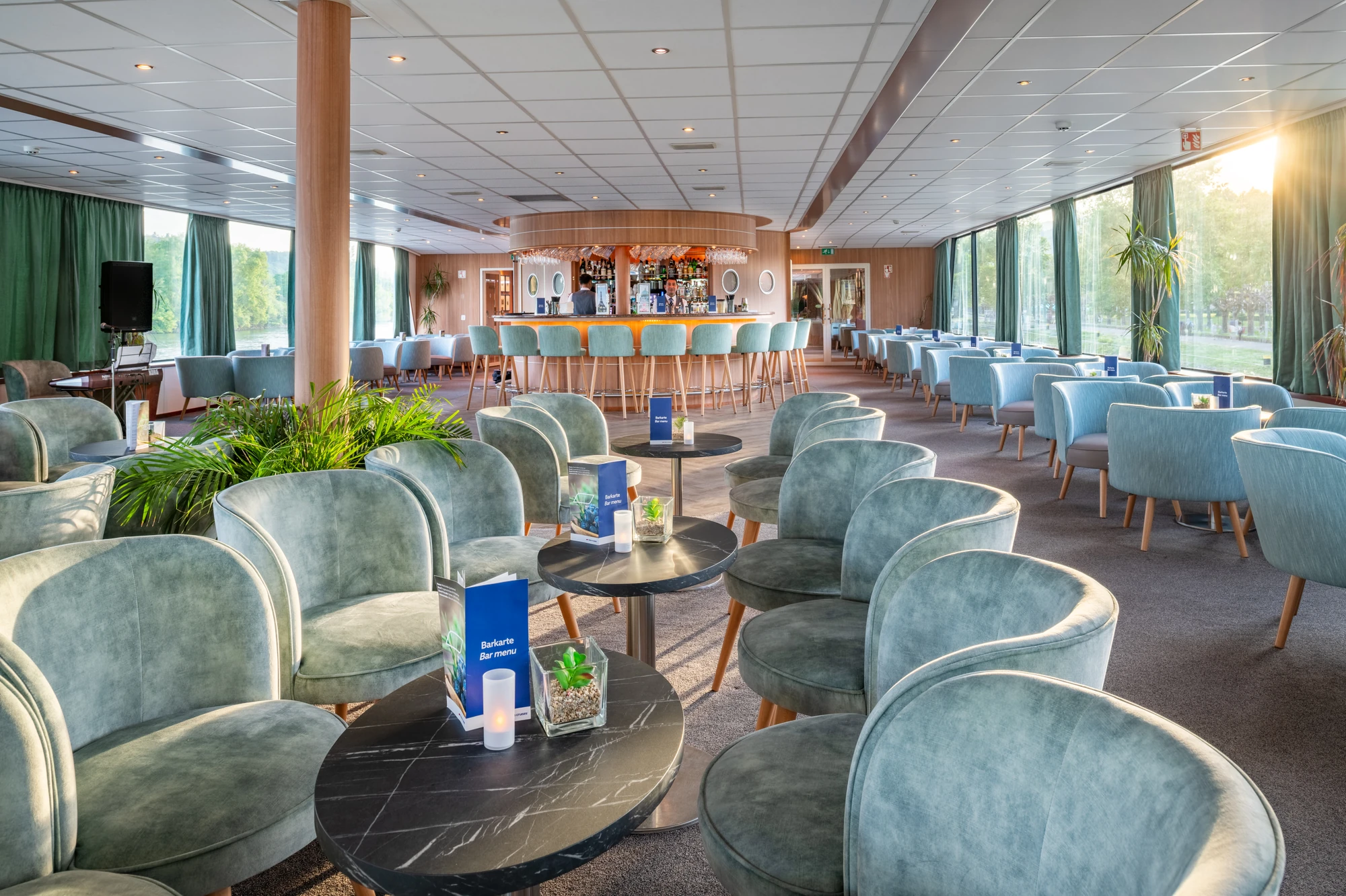 Sitzgelegenheiten mit Tischen und einer Bar im Hintergrund im Salon an Bord der RHEIN MELODIE an einem Anlegeplatz