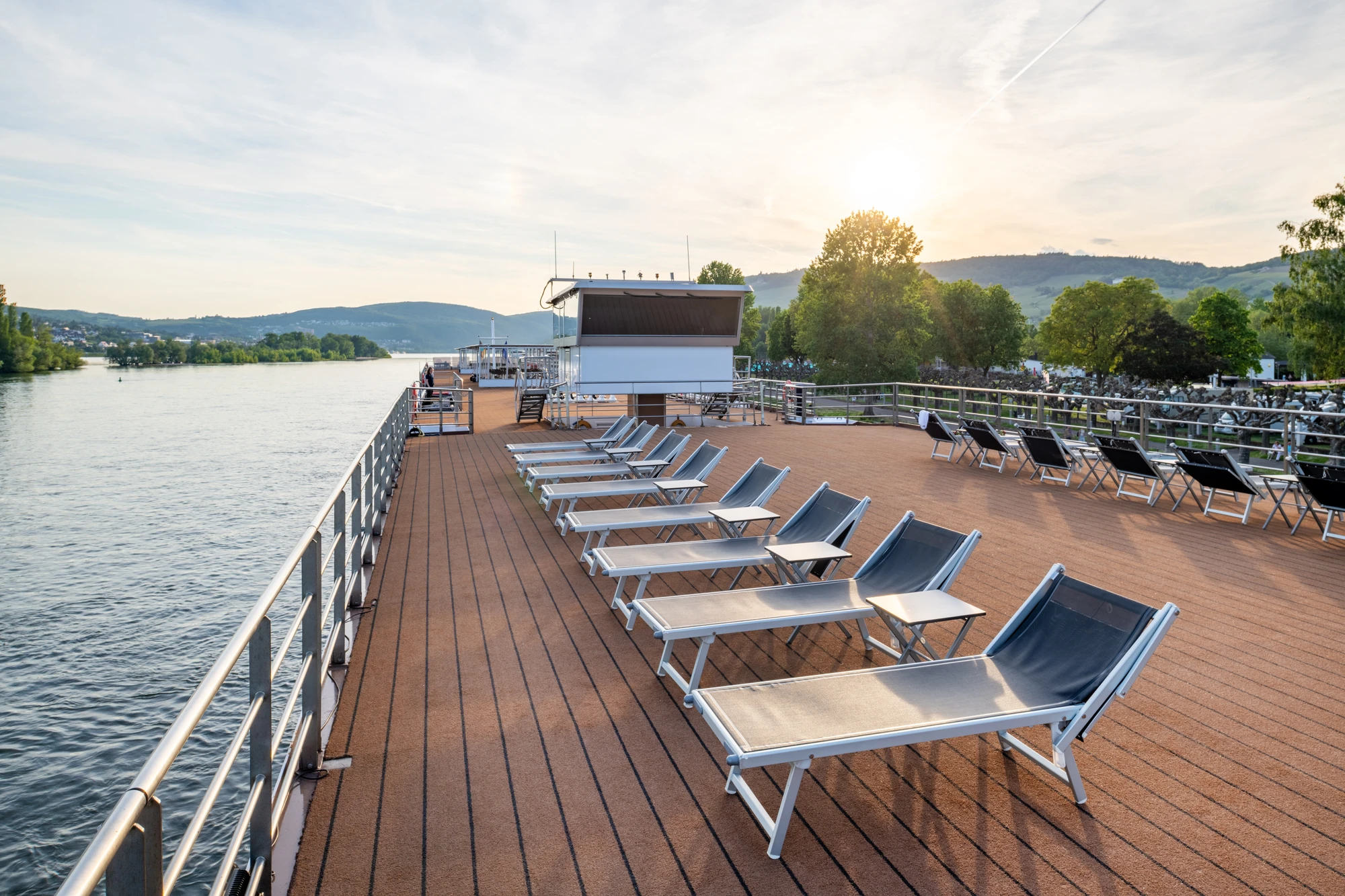 Sonnenliegen auf dem Sonnendeck der RHEIN MELODIE bei Fahrt auf einem Fluss entlang der Ufer mit Bäumen und Sonnenschein