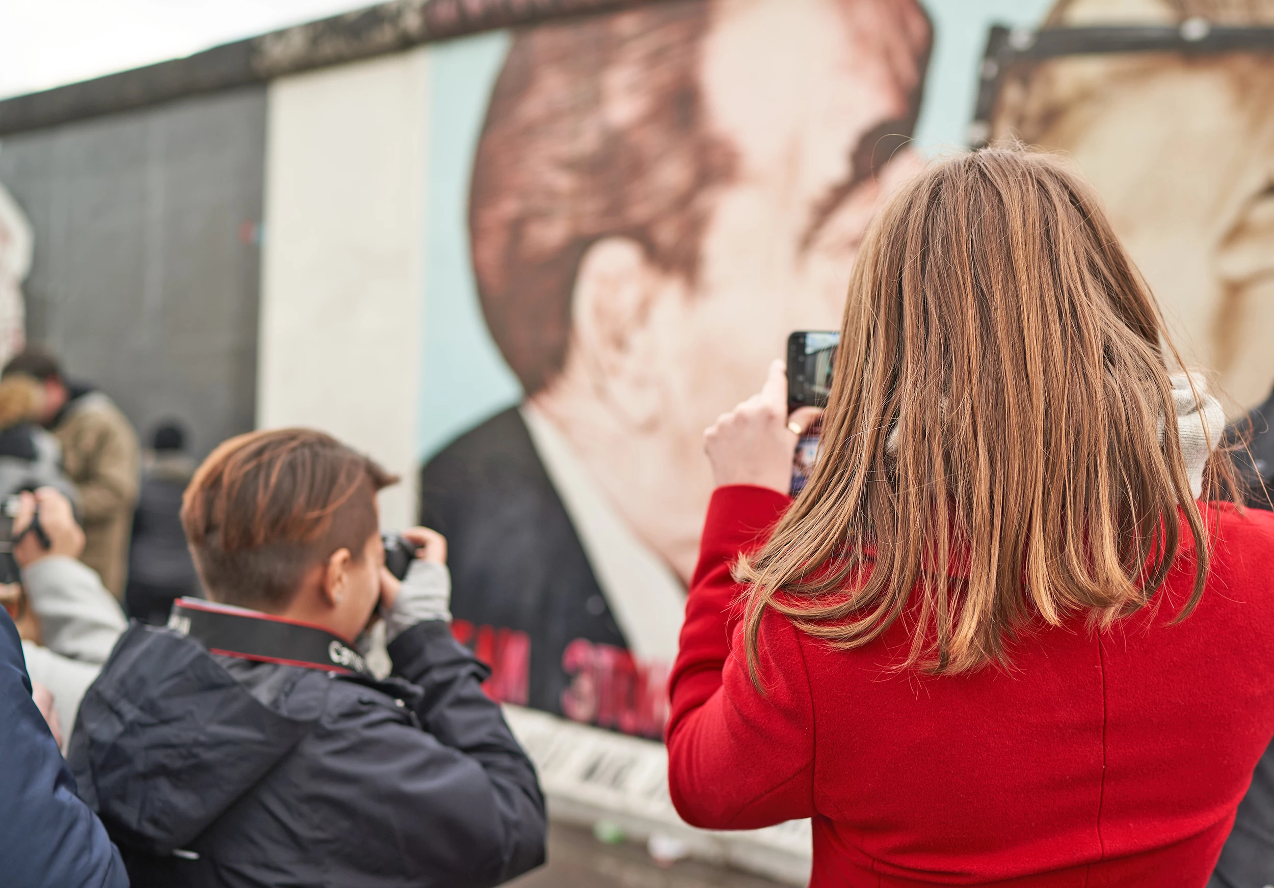 East Side Gallery, Frau beim Kurzurlaub Berlin fotografiert Mauerrest mit Zeichnung vom Kuss Garbatschow und Honecker