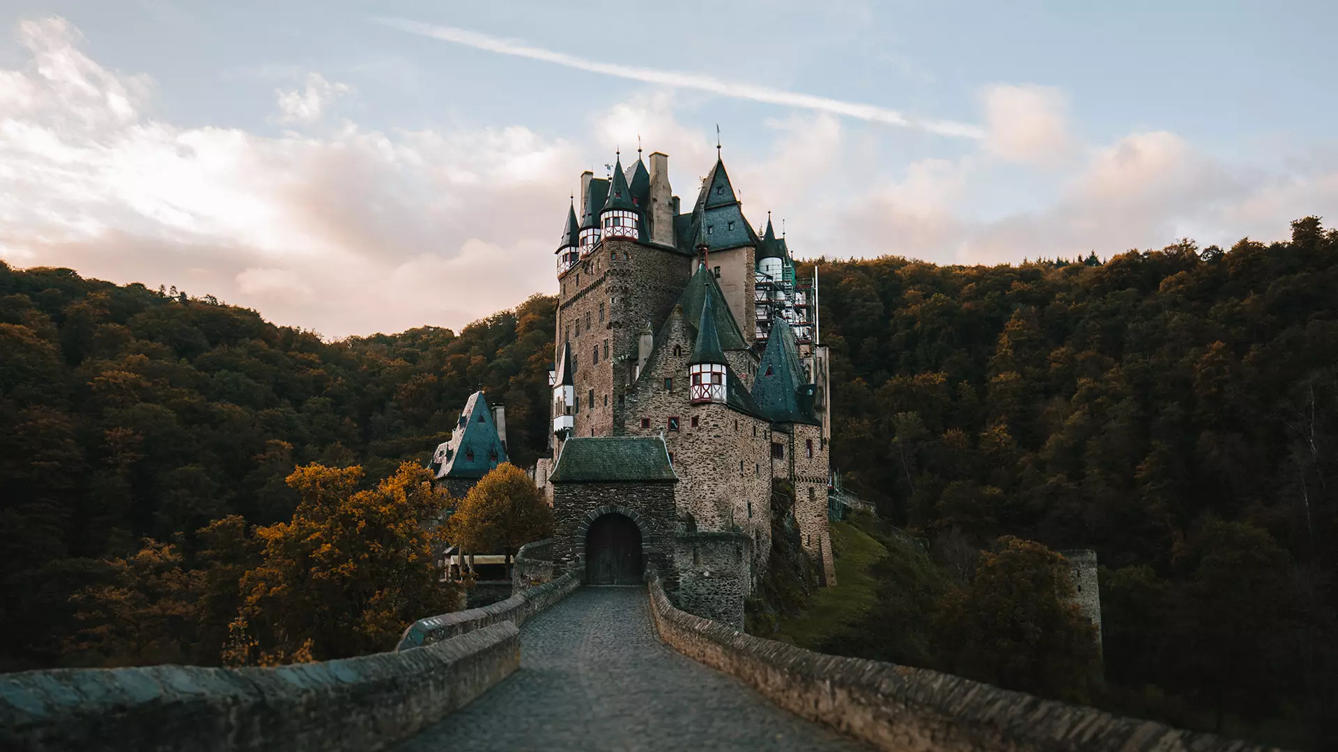 Burg Eltz an der Mosel – Außenansicht vor bewölktem Himmel, durchbrochen von Sonnenstrahlen