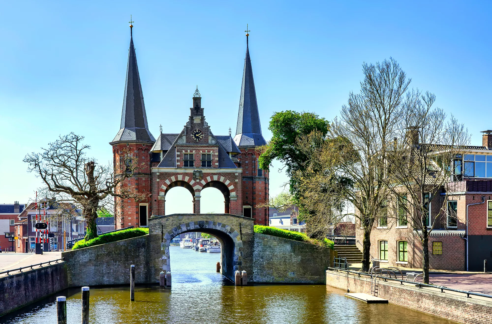 Das alte Wassertor in Sneek mit seinen charakteristischen Türmen, majestätisch am Hafen in Friesland gelegen, bei strahlendem Sonnenschein. Die historische Architektur spiegelt die reiche maritime Geschichte der Stadt wider, während das warme Licht des Tages die Details der Fassade hervorhebt. Diese malerische Szenerie lädt dazu ein, die Schönheit der Umgebung und das Erbe der Region zu genießen.