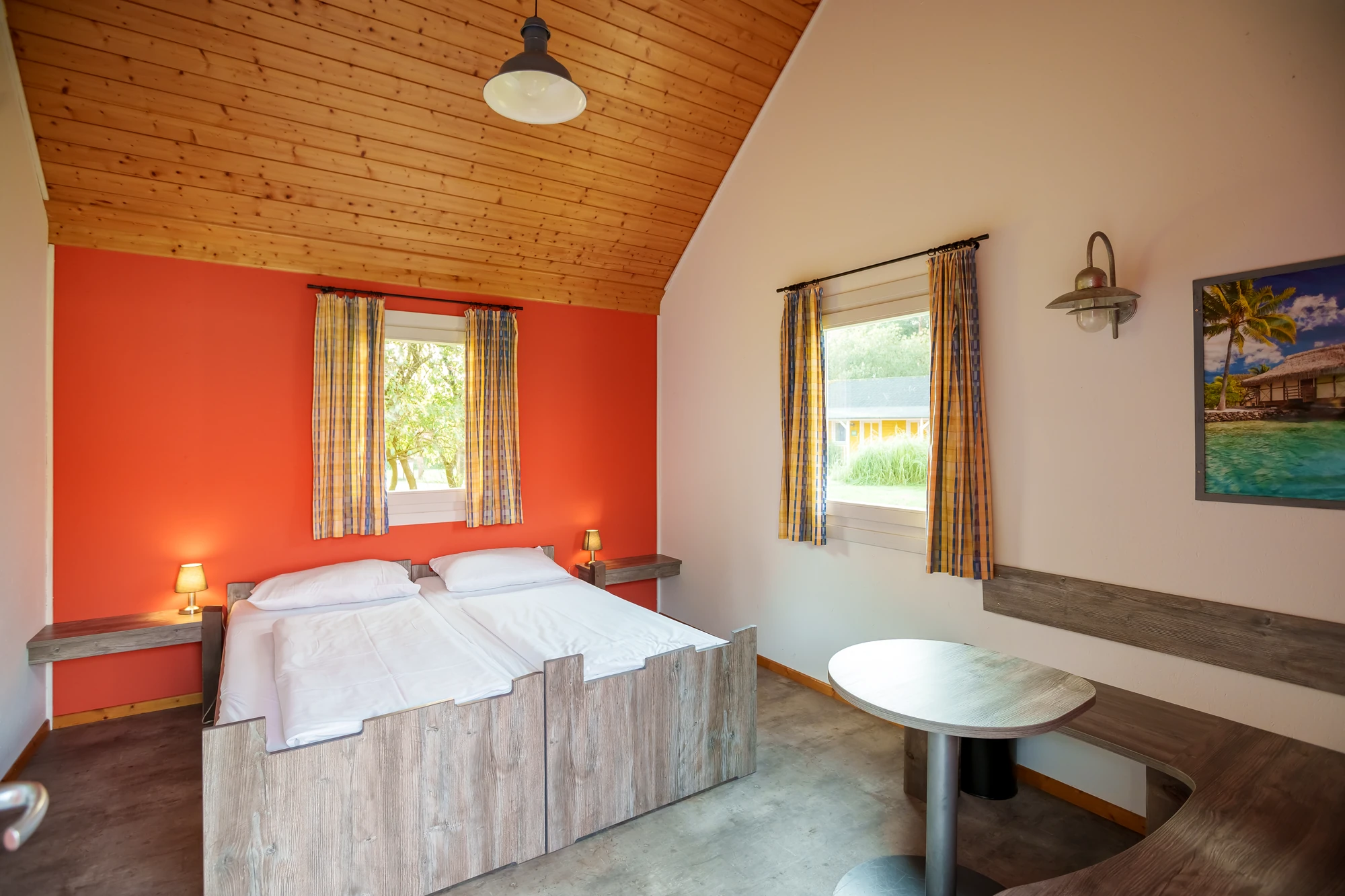 Doppelbett und Sitzecke in einer Holzhütte mit orangefarbener Wand im Holiday Camp