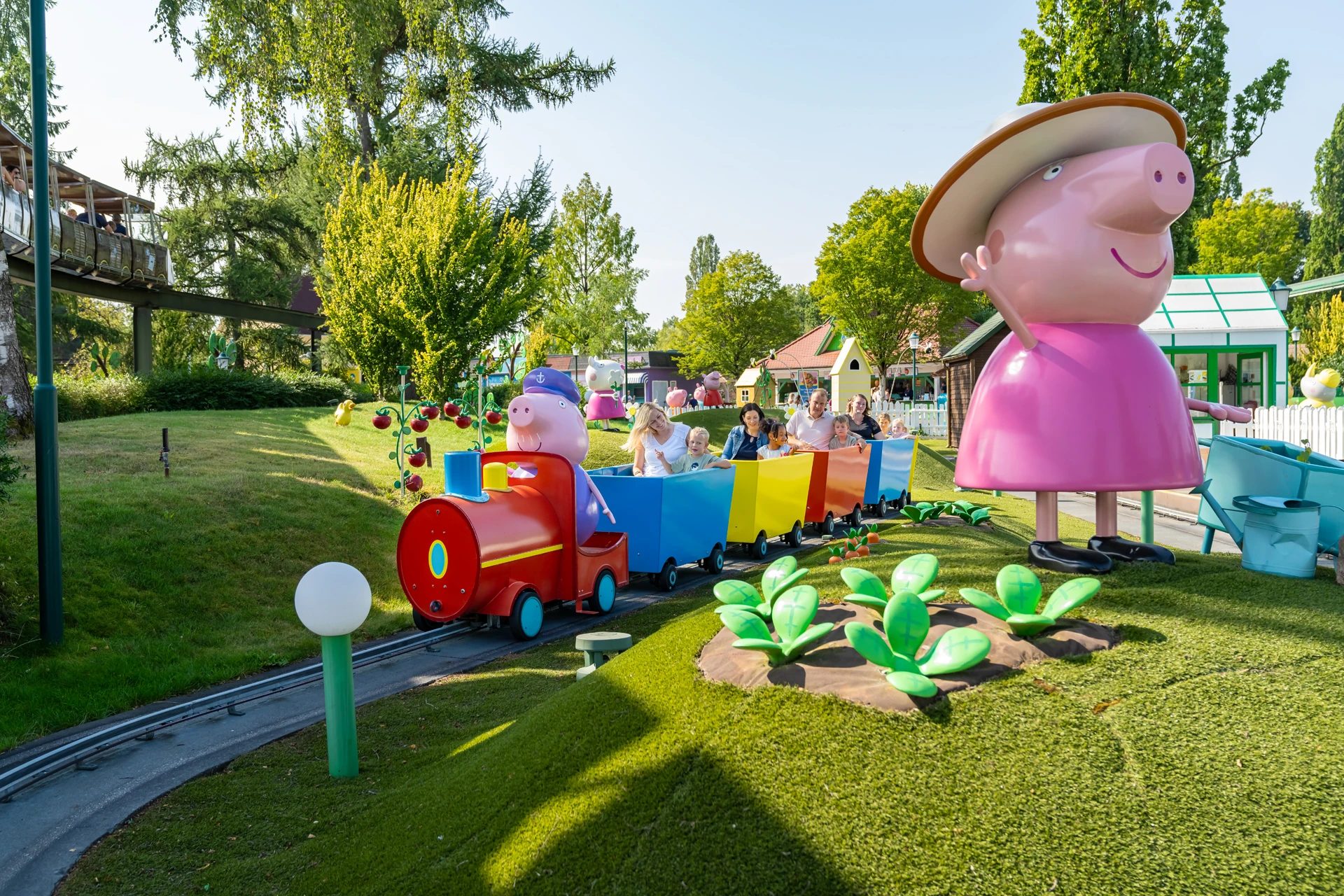 Bunter Zug von Peppa Pig mit bunten Waggons und Menschen darin auf einer Schiene im Heide Park Resort