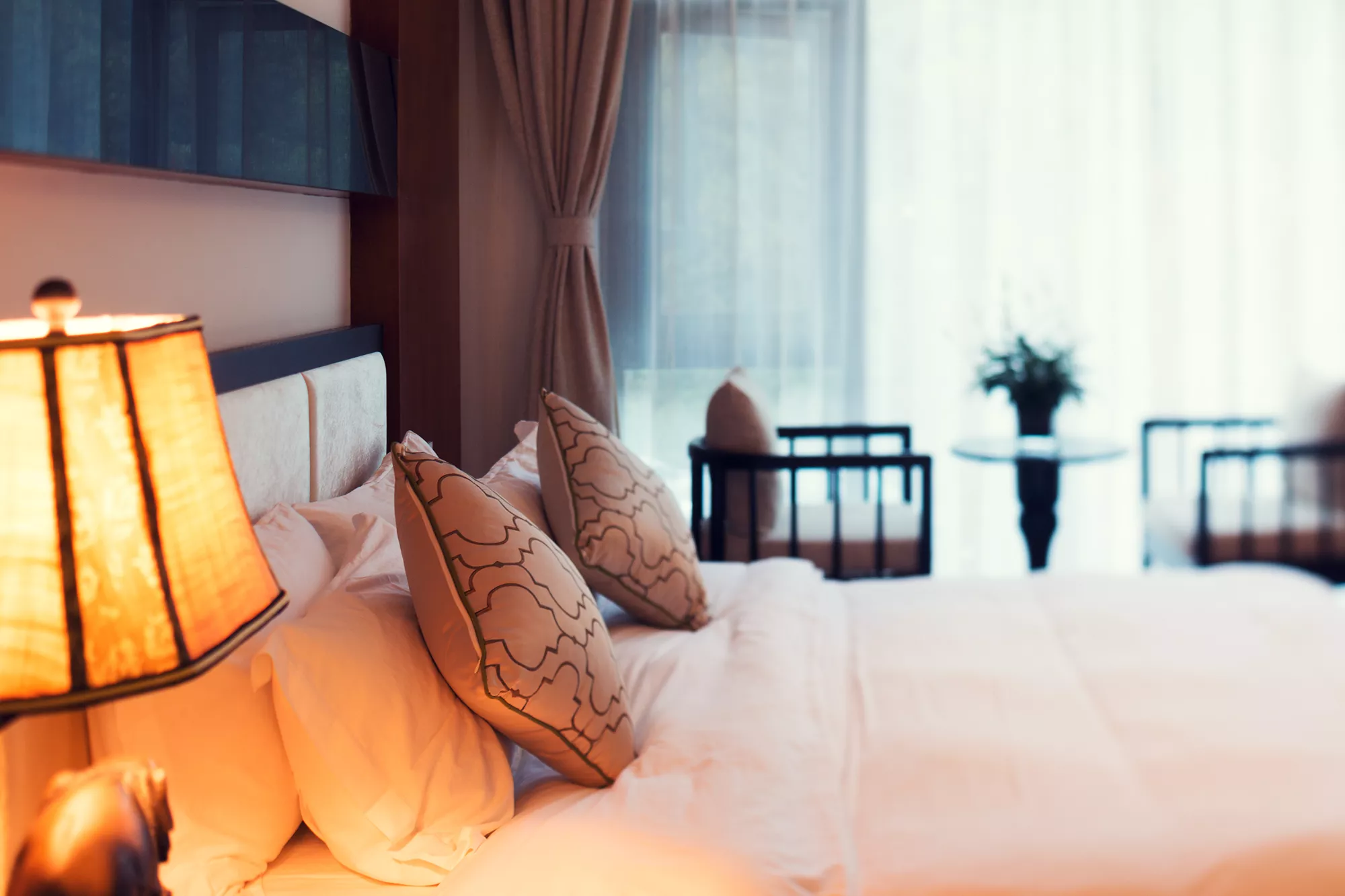 Beispielhotel Zimmerbild mit Doppelbett und verschwommenen Sitzbereich im Hintergrund.