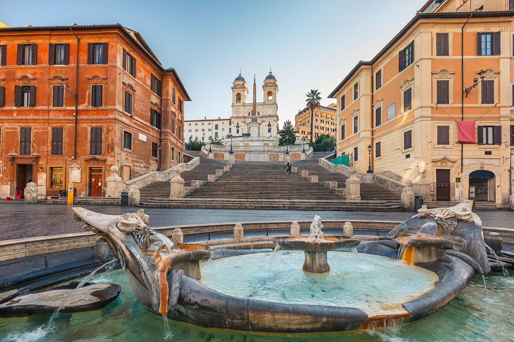 Im Vordergrund die Fontana della Barcaccia, ein malerischer Brunnen, während sich im Hintergrund zwischen den farbenfrohen historischen Gebäuden die Spanische Treppe mit ihren 138 Stufen erhebt. Die harmonische Verbindung von Brunnen und Treppe schafft eine einladende Atmosphäre im Herzen von Rom.