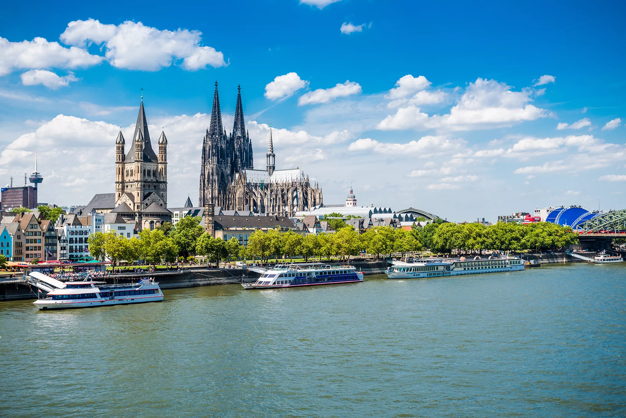 Blick auf den Dom von Köln und die romanische Kirche Groß St. Martin mit Schiffen auf dem Rhein im Vordergrund