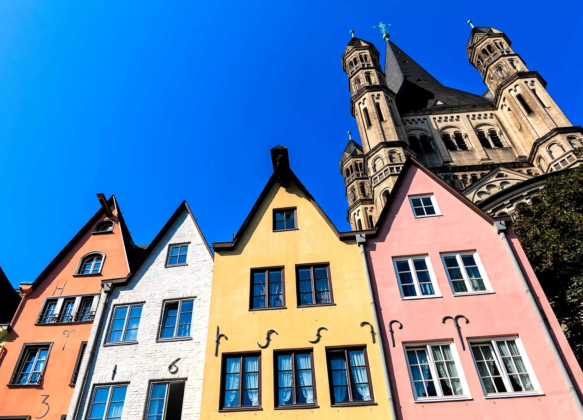 vier bunte Häuser am alten Fischmarkt in der Altstadt von Köln mit der Klosterkirche Groß Sankt Martin im Hintergrund