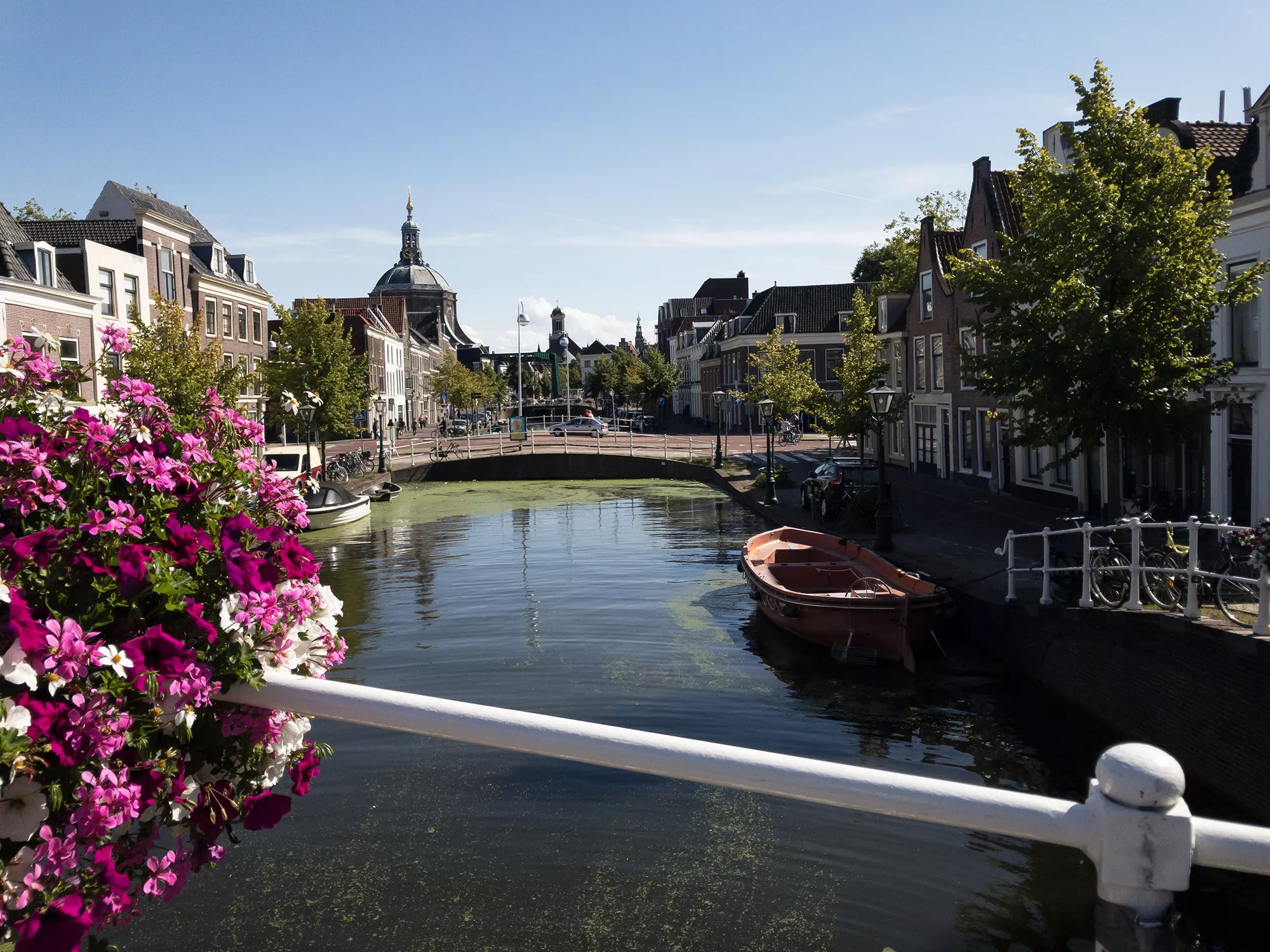 Der Spaarne Kanal in Leiden, erfasst bei Sonnenschein, mit bunten Blumen, die das Ufer säumen. Die lebhaften Farben der Blumen harmonieren mit dem glitzernden Wasser und schaffen eine einladende, fröhliche Atmosphäre. Diese Szenerie vermittelt die Schönheit der Stadt und lädt zum Verweilen und Genießen der Natur ein.