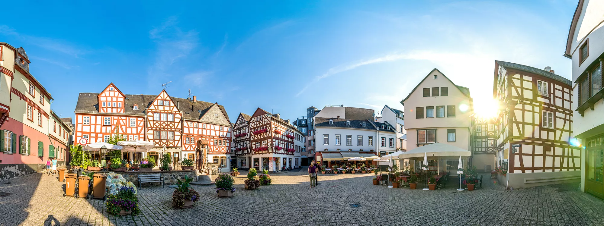 Blick auf einen Marktplatz in Limburg mit Sitzbereichen und aufgespannten Sonnenschirmen. umrandet von Fachwerkhäusern.