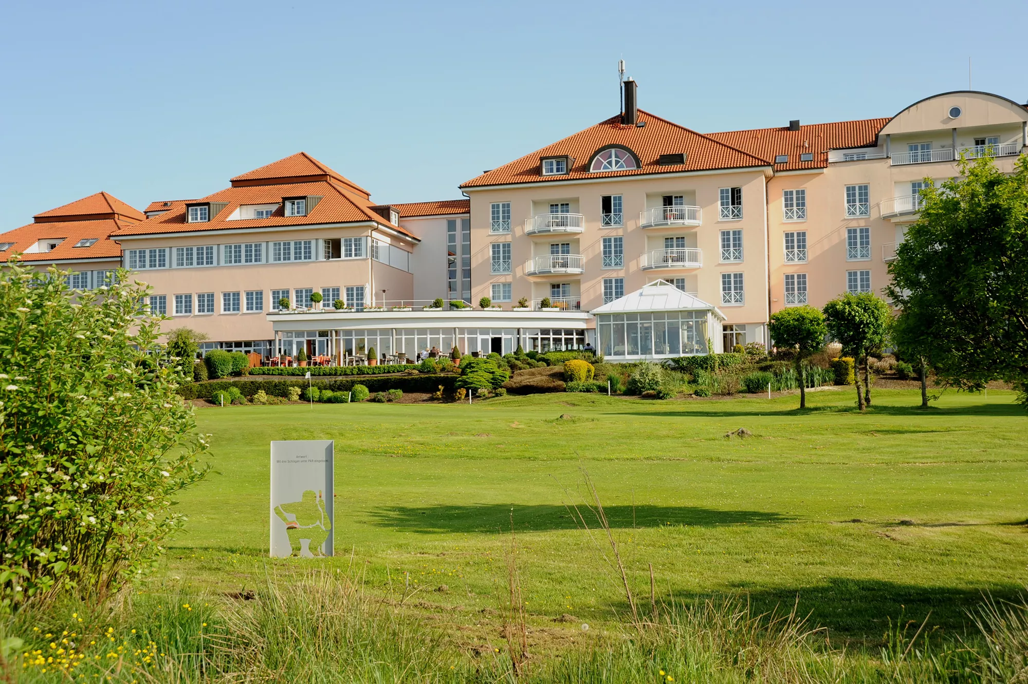 Blick von großzügiger Parkanlage auf die Rückseite des Golf & Sporthotel Wiesensee
