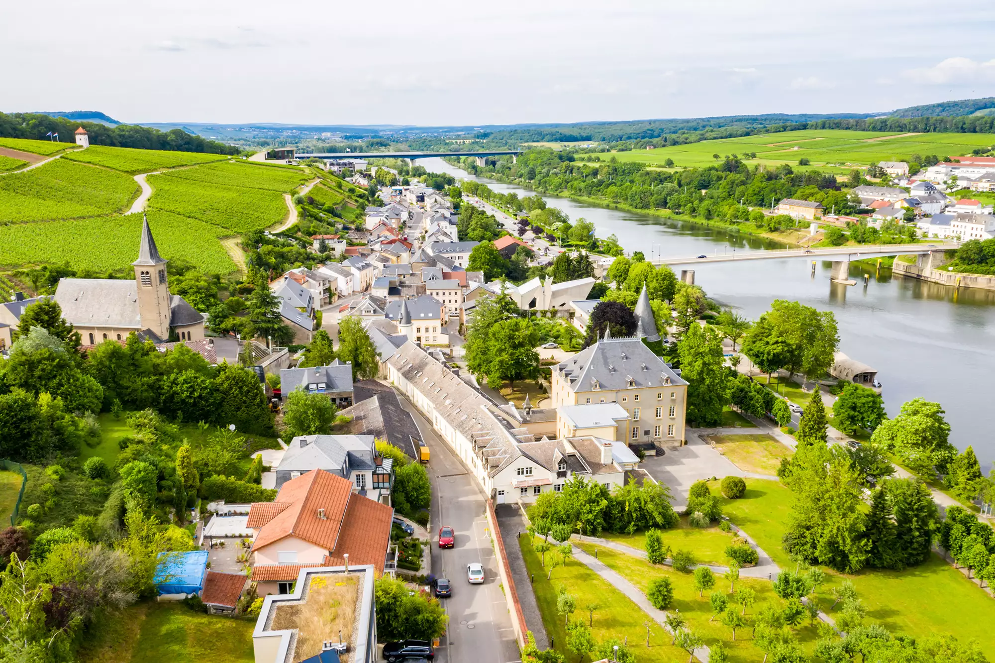 Panoramablick auf Schengen an der Mosel in Luxemburg bei Tageslicht. Die malerische Landschaft, die sanften Hügel und das ruhige Wasser verleihen der Szene eine friedliche und einladende Atmosphäre.