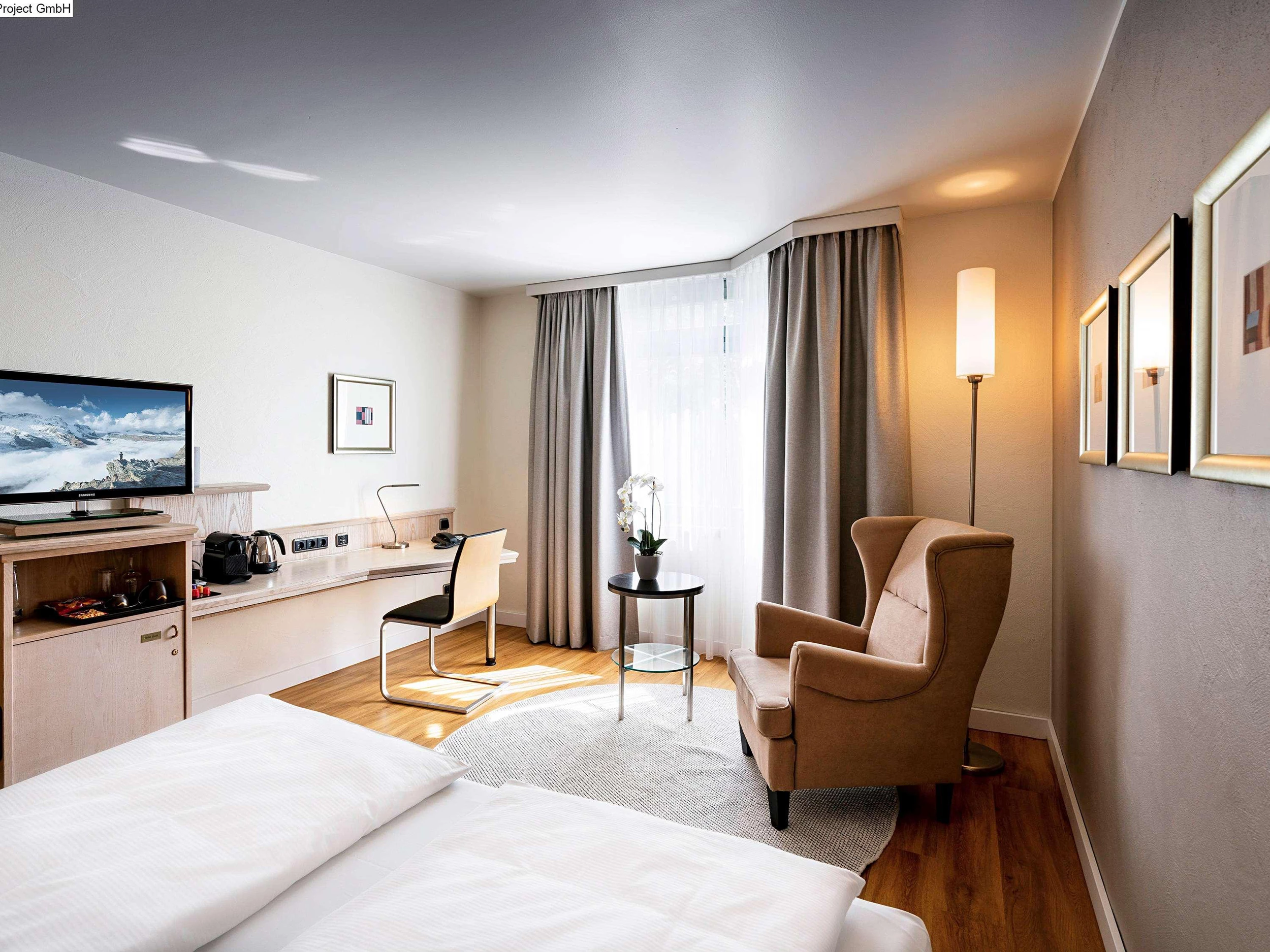 Zimmerbeispiel im Mövenpick Hotel München Airport mit Doppelbett, Fernseher, Schreibtisch und Ohrensessel