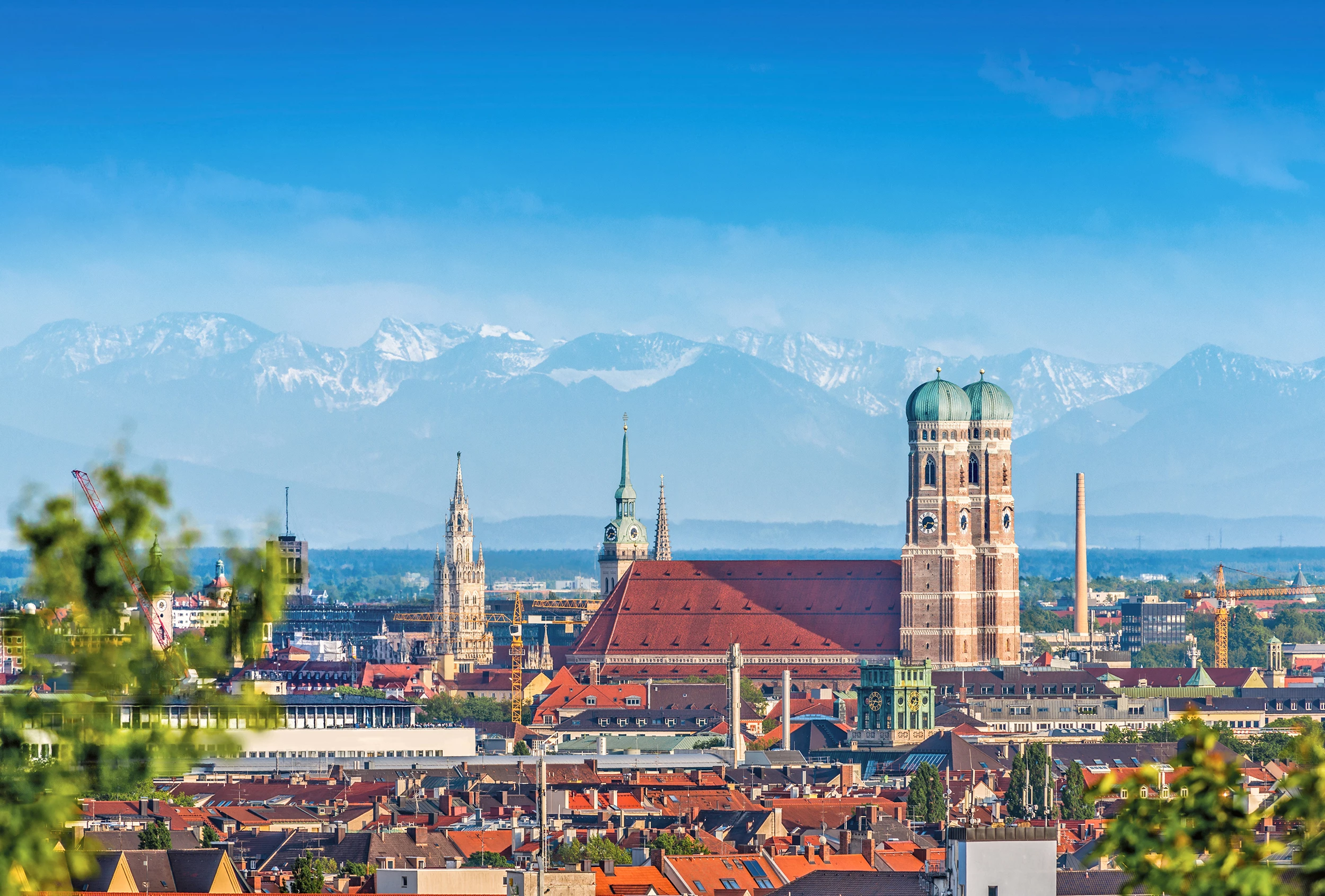Frauenkirche bei blauem Himmel und klarer Sicht auf die Alpen bei Bahn und Hotel München