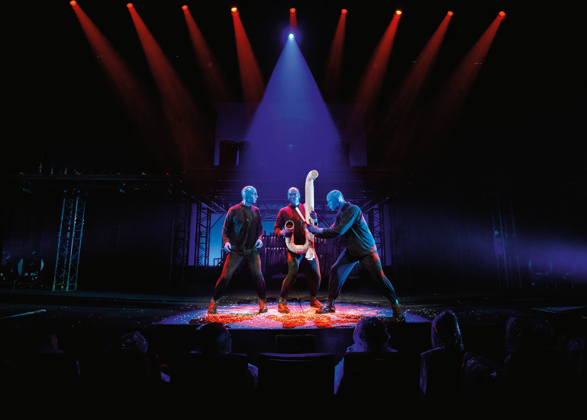 Blue Man Group Show in Berlin -Szene 3 blaue Männer in schwarzer Kleidung stehen im Scheinwerferlicht auf der Bühne