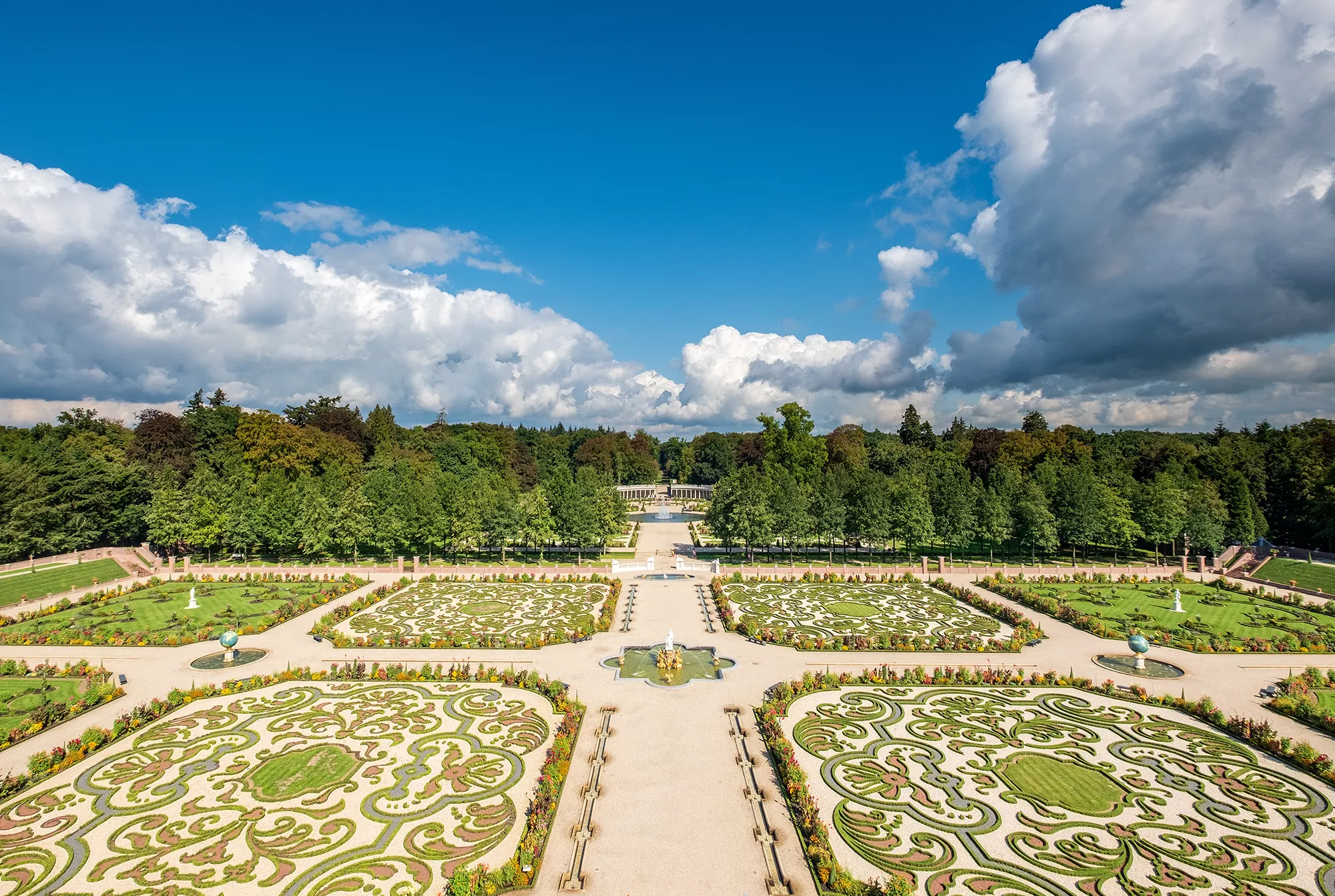 Der Garten von Het Loo, ein wunderschön gepflegter Barockgarten in Apeldoorn, bei sattem Tageslicht. Die prächtigen Blumenbeete, kunstvoll angelegten Wege und klassizistischen Skulpturen schaffen eine harmonische und einladende Atmosphäre, die die Pracht des Gartens unterstreicht.