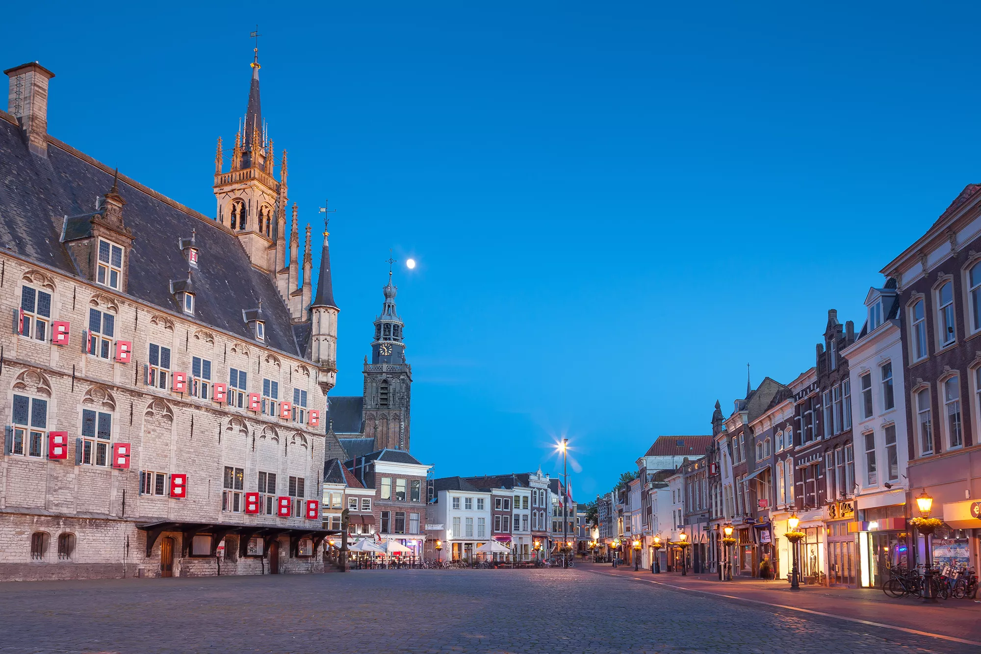 Das Rathaus von Gouda am Marktplatz in der Abenddämmerung, beleuchtet von sanften Stadtlichtern. Die warme Beleuchtung hebt die architektonischen Details des historischen Gebäudes hervor und schafft eine romantische Atmosphäre. Die Kombination aus Dämmerung und Stadtbeleuchtung verleiht der Szene eine einladende und magische Stimmung, die das Flair der Stadt perfekt einfängt.