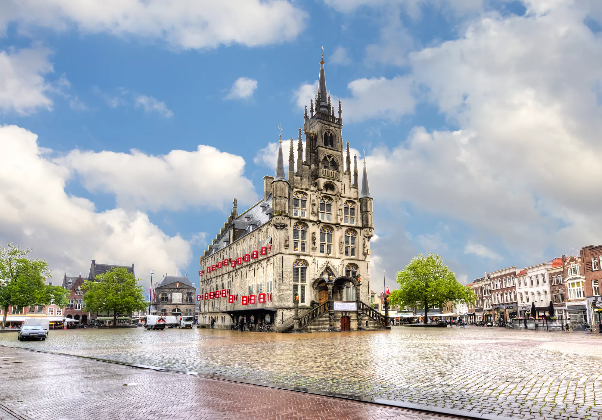 Das Rathaus am Marktplatz in Gouda, erfasst bei hellem Tageslicht. Die beeindruckende Fassade des historischen Gebäudes strahlt im Sonnenlicht, während der lebhafte Marktplatz mit seinen umgebenden Cafés und Geschäften eine einladende Atmosphäre schafft. Diese Szenerie verkörpert das charmante Flair der Stadt und lädt zum Verweilen ein.