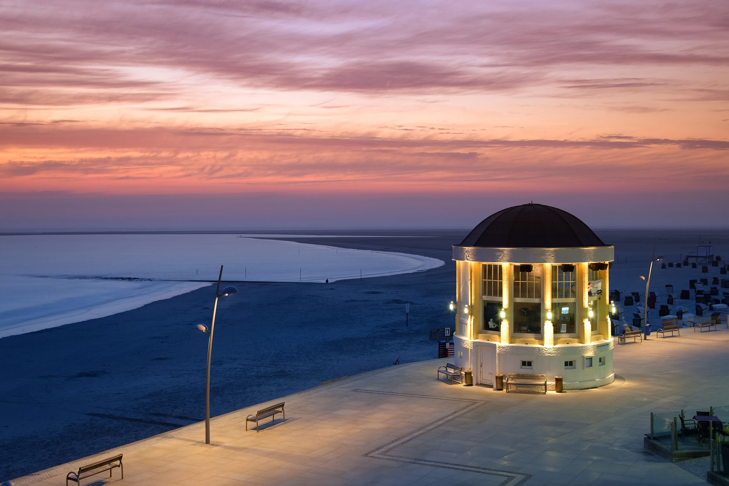 Musikpavillon an der Promenade in Borkum mit Blick auf einen rosa Sonnenuntergang über der Nordsee beim Urlaub am Wasser