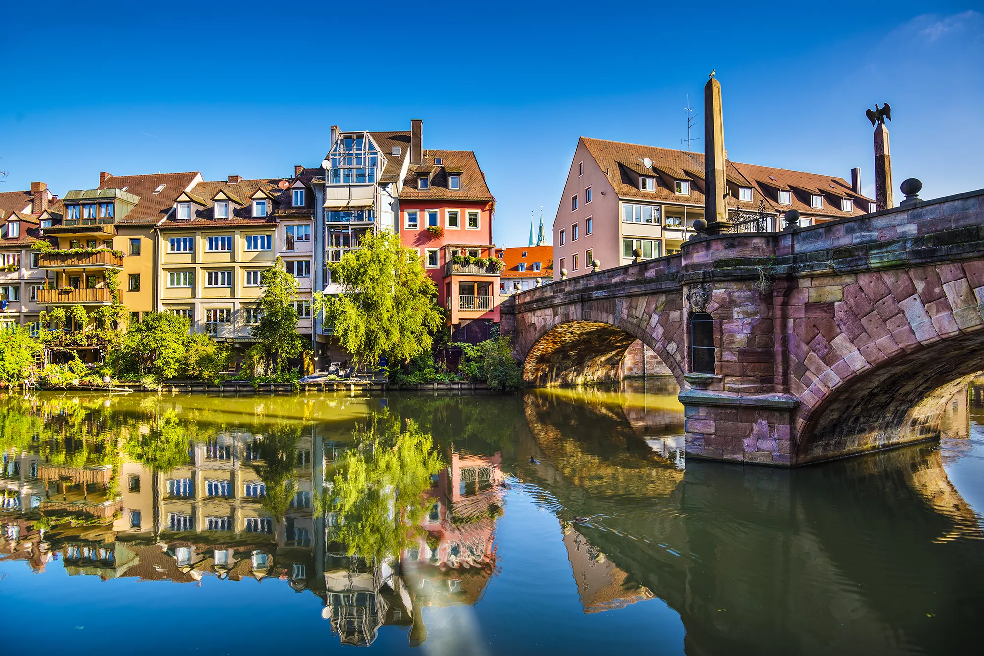 Bunte Wohnhäuser und die Maxbrücke spiegeln sich im Wasser der Pegnitz in Nürnberg