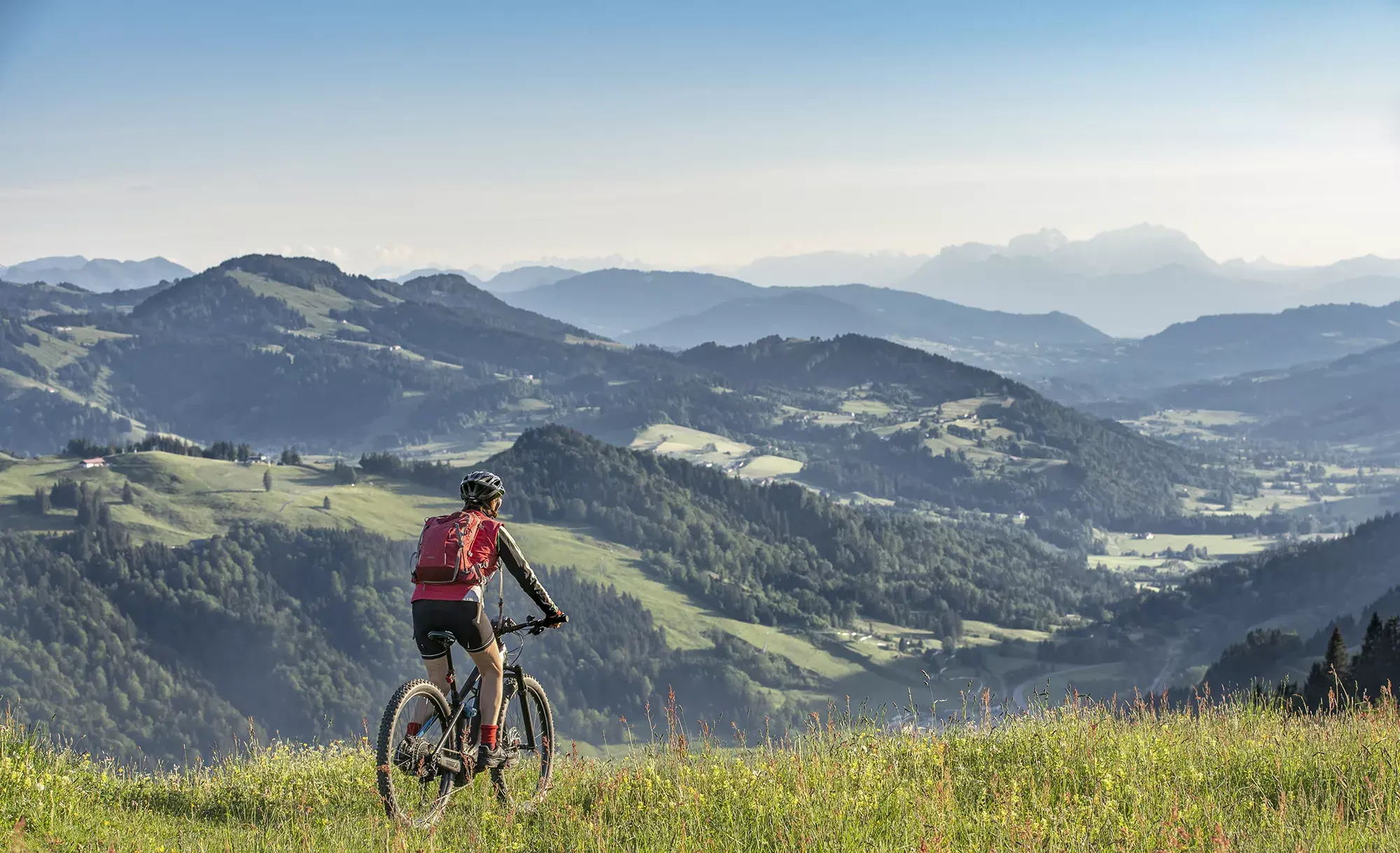 Panoramabild auf die Allgäuer Landschaft mit grünen Bergen und einem, die Aussicht geniesenden Mountainbike Fahrer