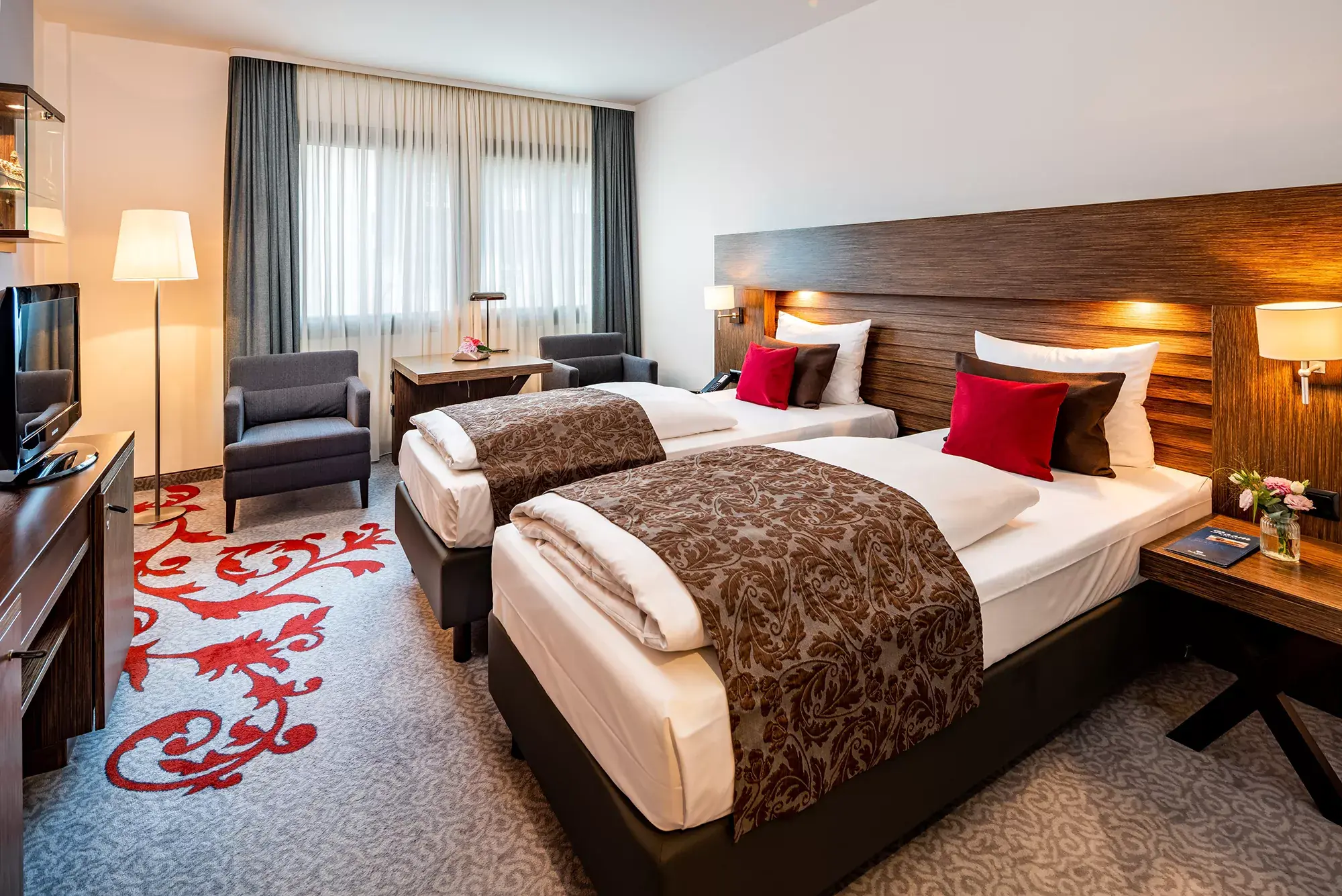 Doppelzimmer Comfort (Beispiel) im Park Plaza Hotel Trier - Zwei Queensizebetten mit braunem Brokatüberwurf, Sitzecke und Fernseher.