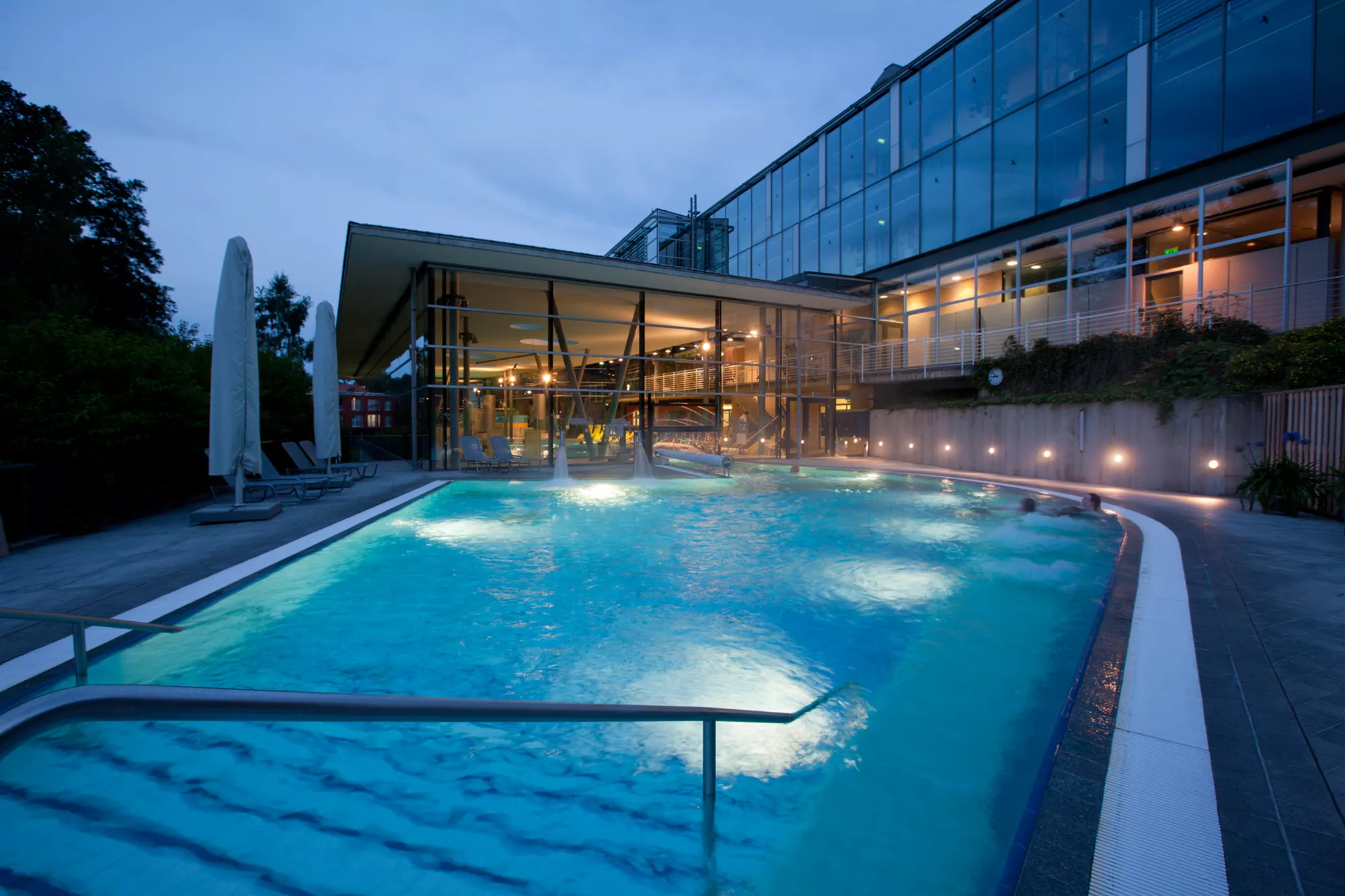 Abbildung des Poolbereiches im Santé Royale Hotel in Bad Brambach mit großem beleuchtetet Außenpool in der Abenddämmerung