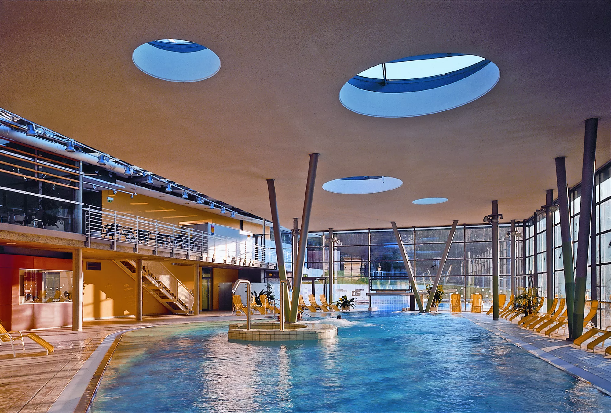 Abbildung des Poolbereiches im Santé Royale Hotel in Bad Brambach mit großem Innenpool, Relaxe Liegen und einer Galerie mit Sitzgruppen