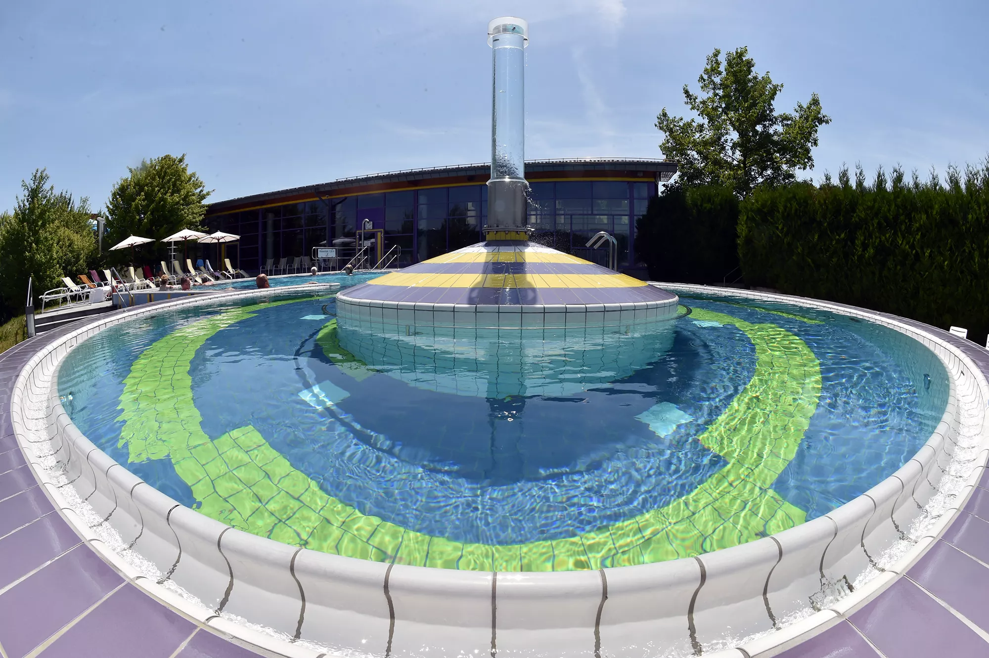 Blick auf den Außenpool im Santé Royale Wolkenstein umrandet von grünen Pflanzen und Bereich mit Sonnenliegen