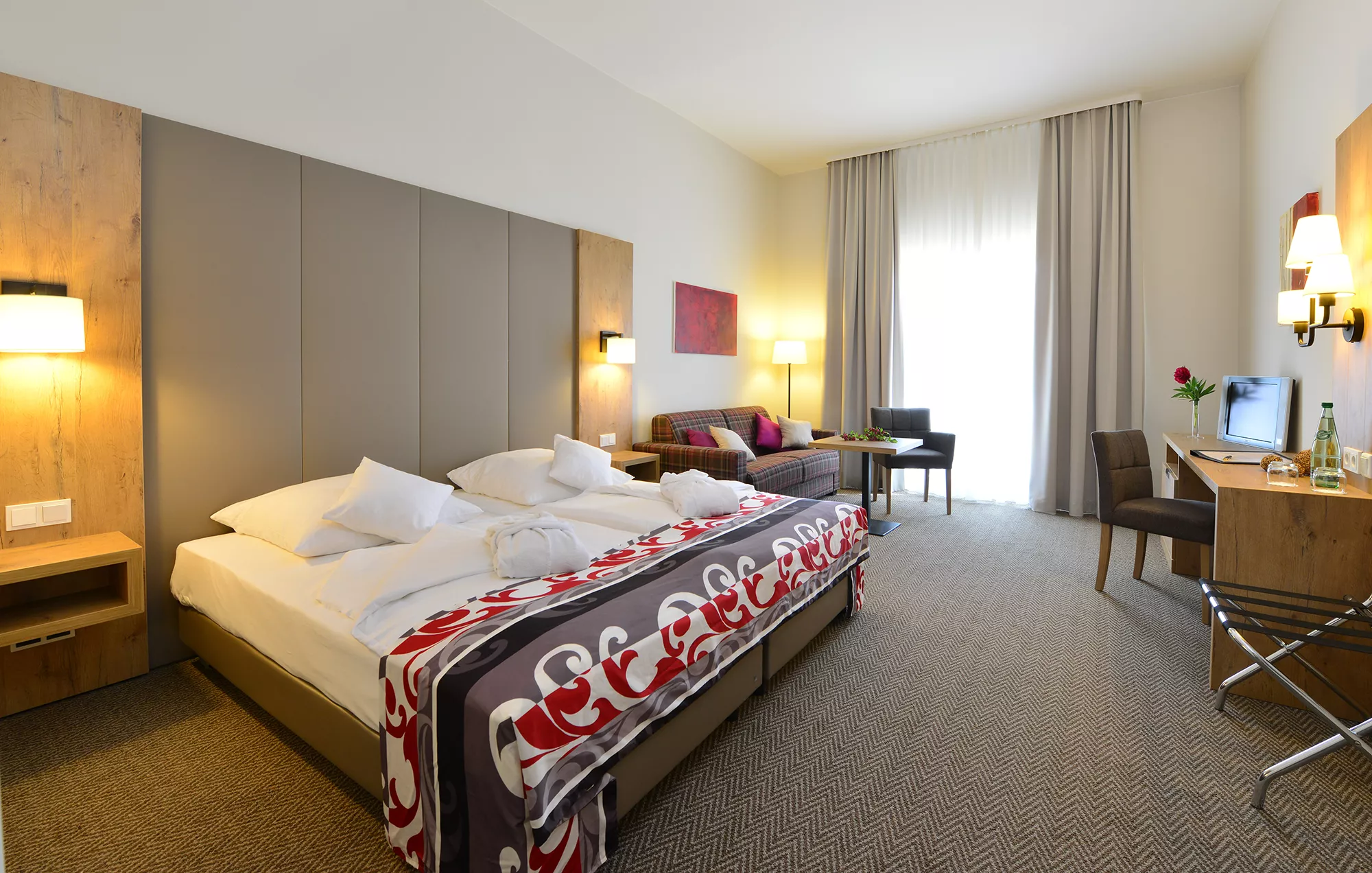 Blick in ein Zimmerbeispiel im Santé Royale Wolkenstein mit großen Doppelbett, Sitzbereich, Schreibtisch, Fernseher