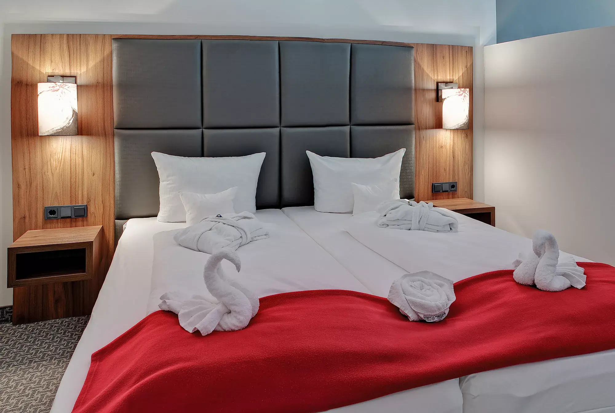 Zimmerbeispiel mit Doppelbett, eine rote Überdecke mit 2 Handtuchschwänen liegt über dem Fußbereich im Sane Royale Hotel Bad Langensalza