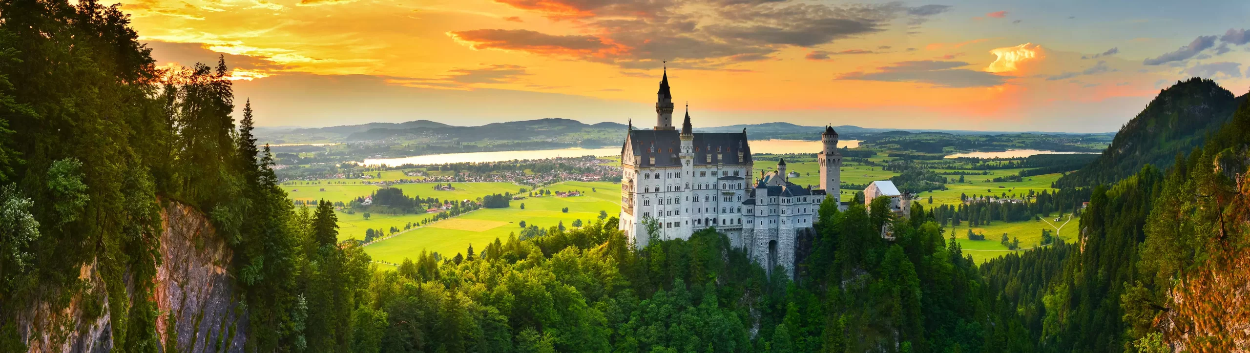 Schloss Neuschwanstein Panorama mit umliegenden Bergen und Wald bei Sonnenuntergang