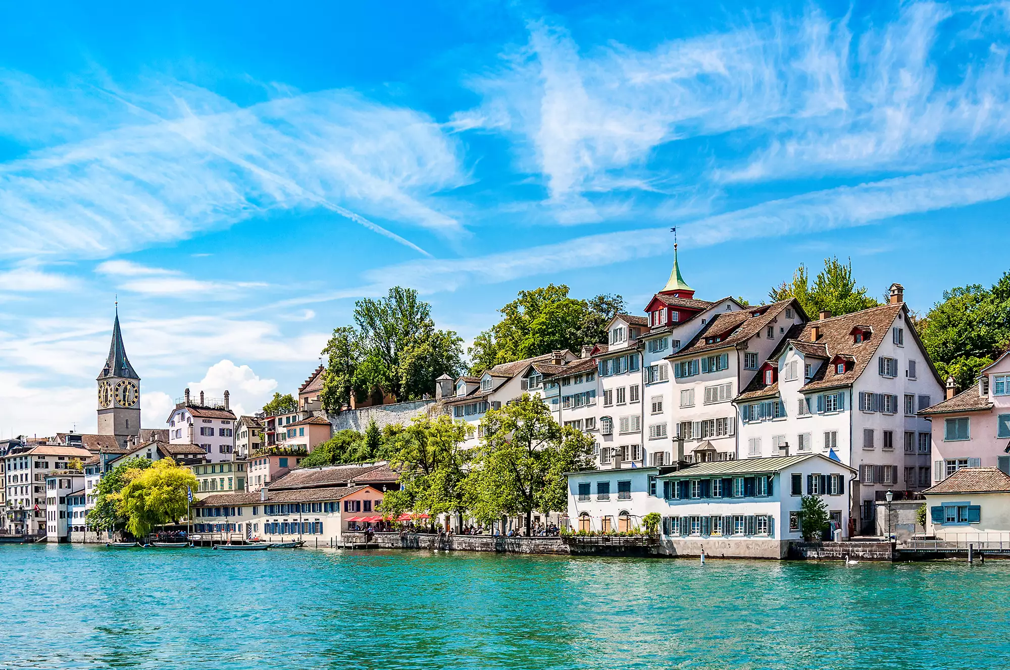 Peterskirche und Wohnhäuser am Ufer des blaugrünen Flusses Limmat in Zürich