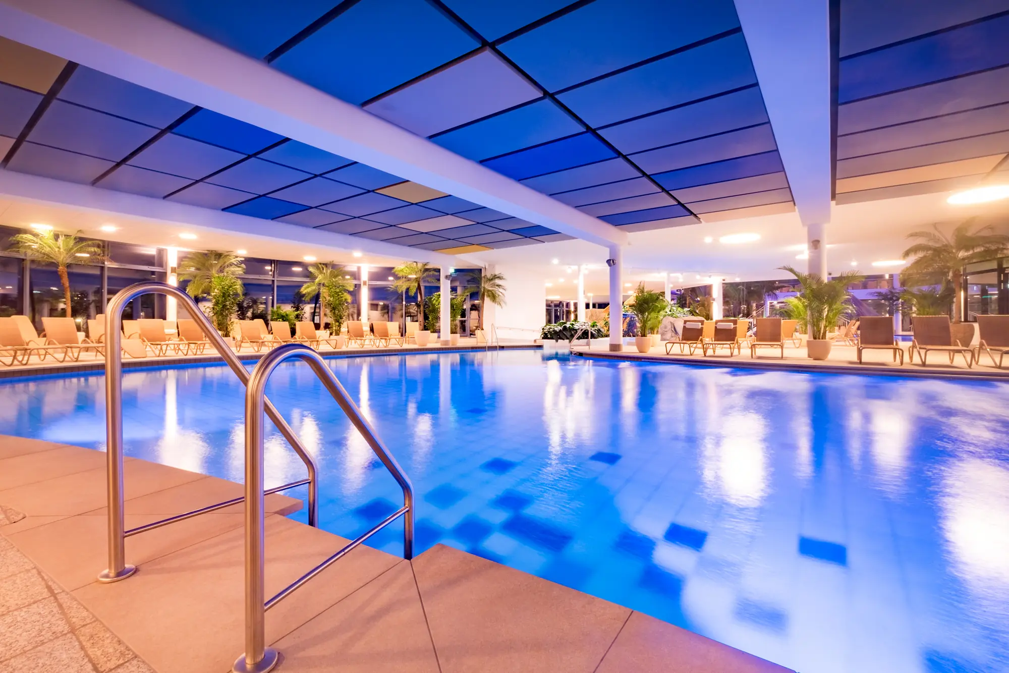 Blick auf das mit Thermalwasser gefüllte, mit Palmen und Liegen umgebene Aktivbecken in der Siebenquell Therme des Wellnesshotel