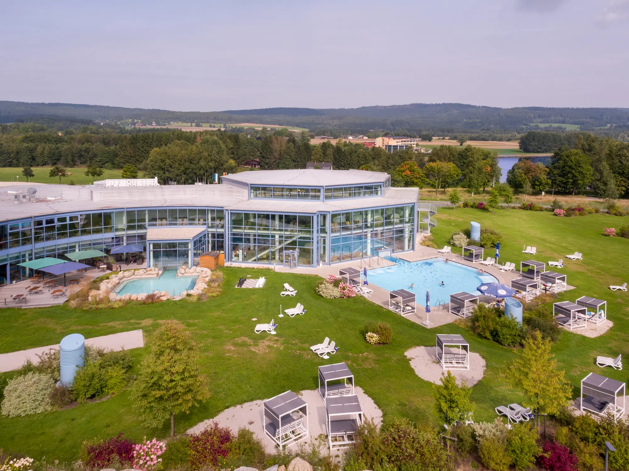 Panoramablick auf den gesamten Außenpoolbereich der Siebenquell Therme mit Liegewiese, Sonnenterrasse mit Liegemöbeln und zwei Wasserbecken