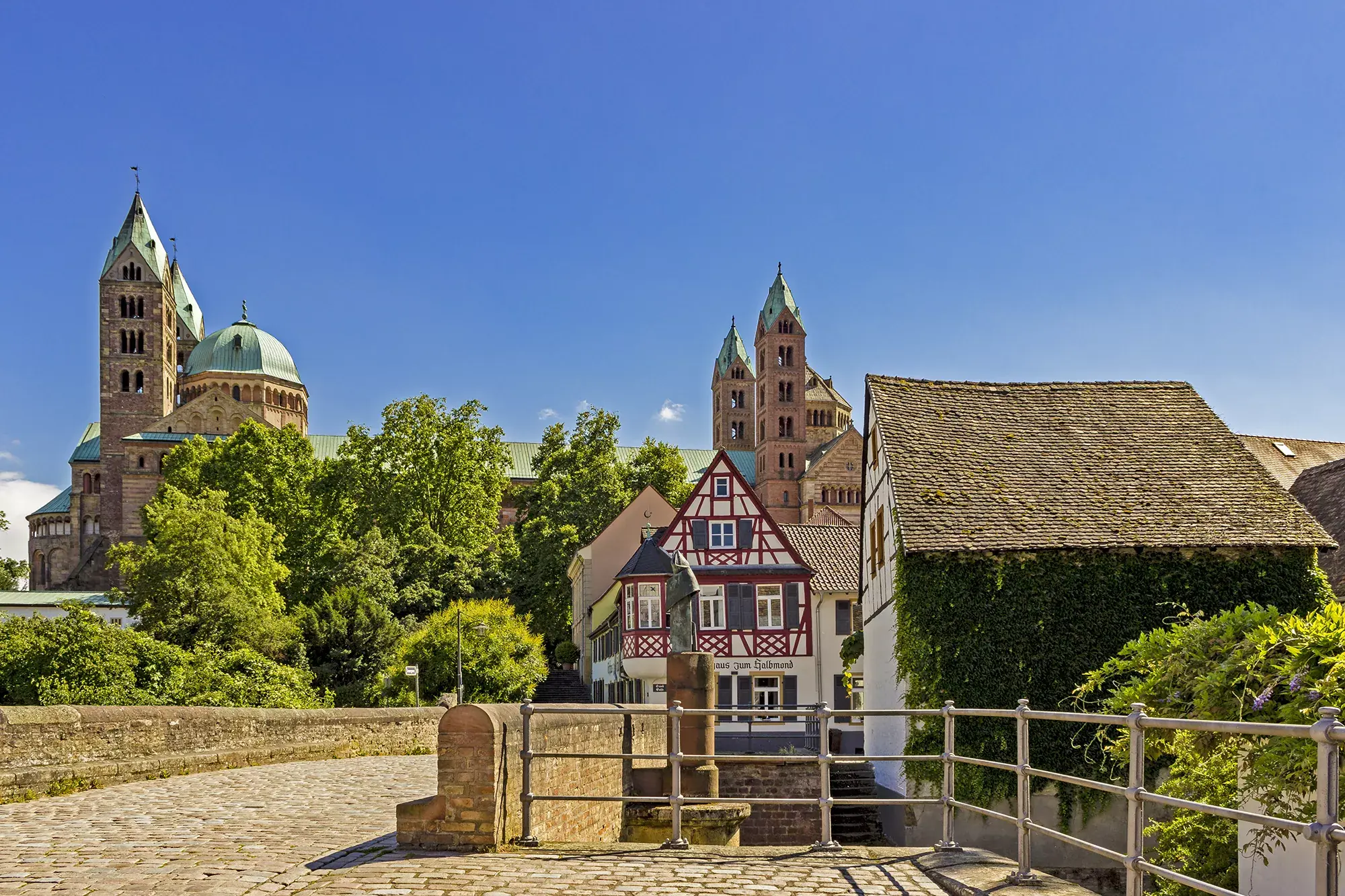 Panoramablick auf den Dom zu Speyer und Fachwerkhäusern von einer mit Kopfstein bepflasterten Brücke an einem sonnigen Tag
