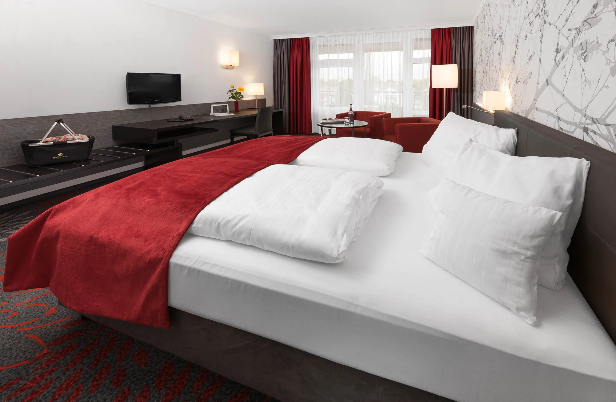 SI Suites Stuttgart – Zimmerbeispiel mit Doppelbett, Sitzecke und Schreibtisch mit TV