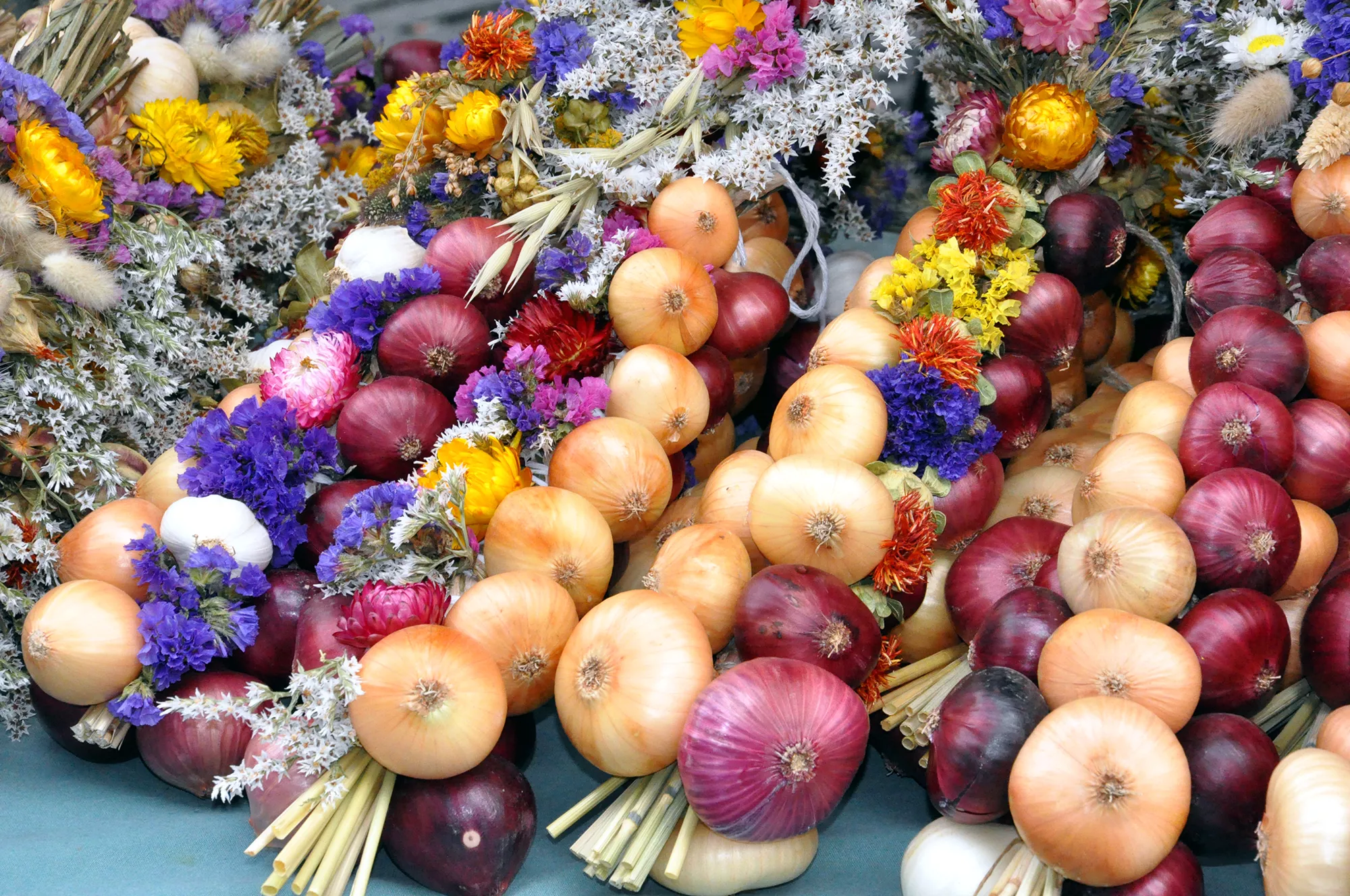 Zwiebelzöpfe aus gelben und roten Zwiebeln und bunten Blumen auf dem Markt von Weimar
