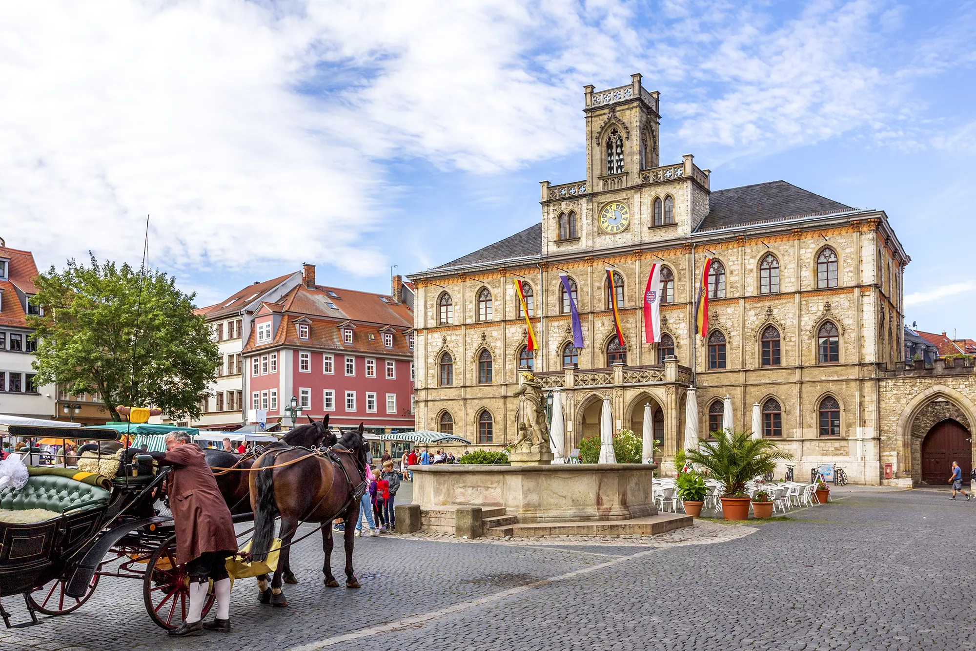 Pferdekutsche vor dem Rathaus Weimar bei schönem Wetter und im Hintergrund der Wochenmarkt bei einer Städtereise in Weimar.