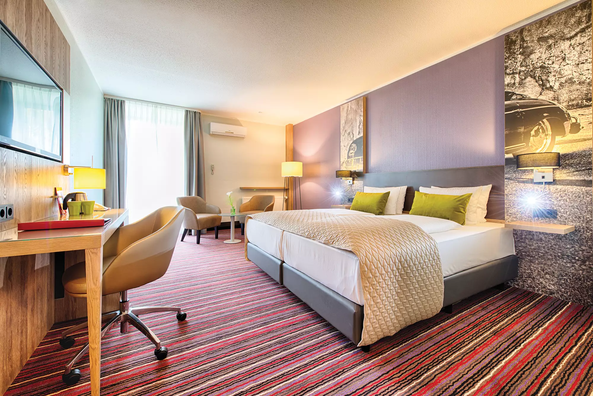 Helles geräumiges Zimmerbeispiel im Leonardo Hotel Wolfsburg mit Doppelbett, Schreibtisch und Fernseher