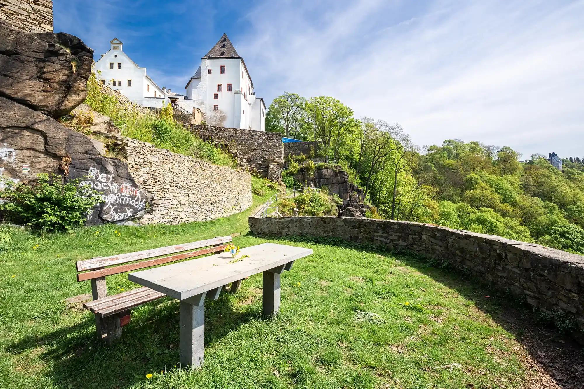 Aussichtspunkt mit einer Bank und Tisch an der Schlossmauer des Schloss Wolkenstein im Erzgebirge und dem aufragendenden Schloss im Hintergrund