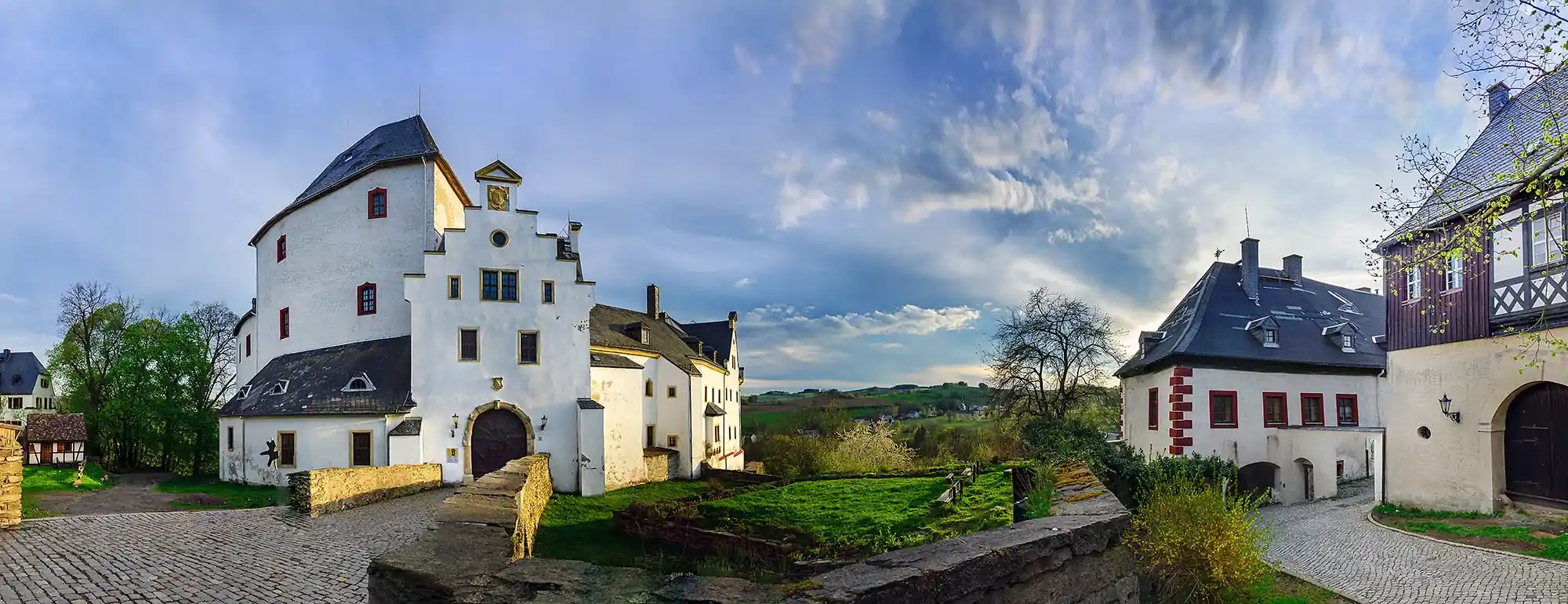 Blick auf weiß gestrichenen Schlossflügel mit schlichten Schieferdächer und Schlossgraben des Schloss Wolkenstein im Erzgebirge