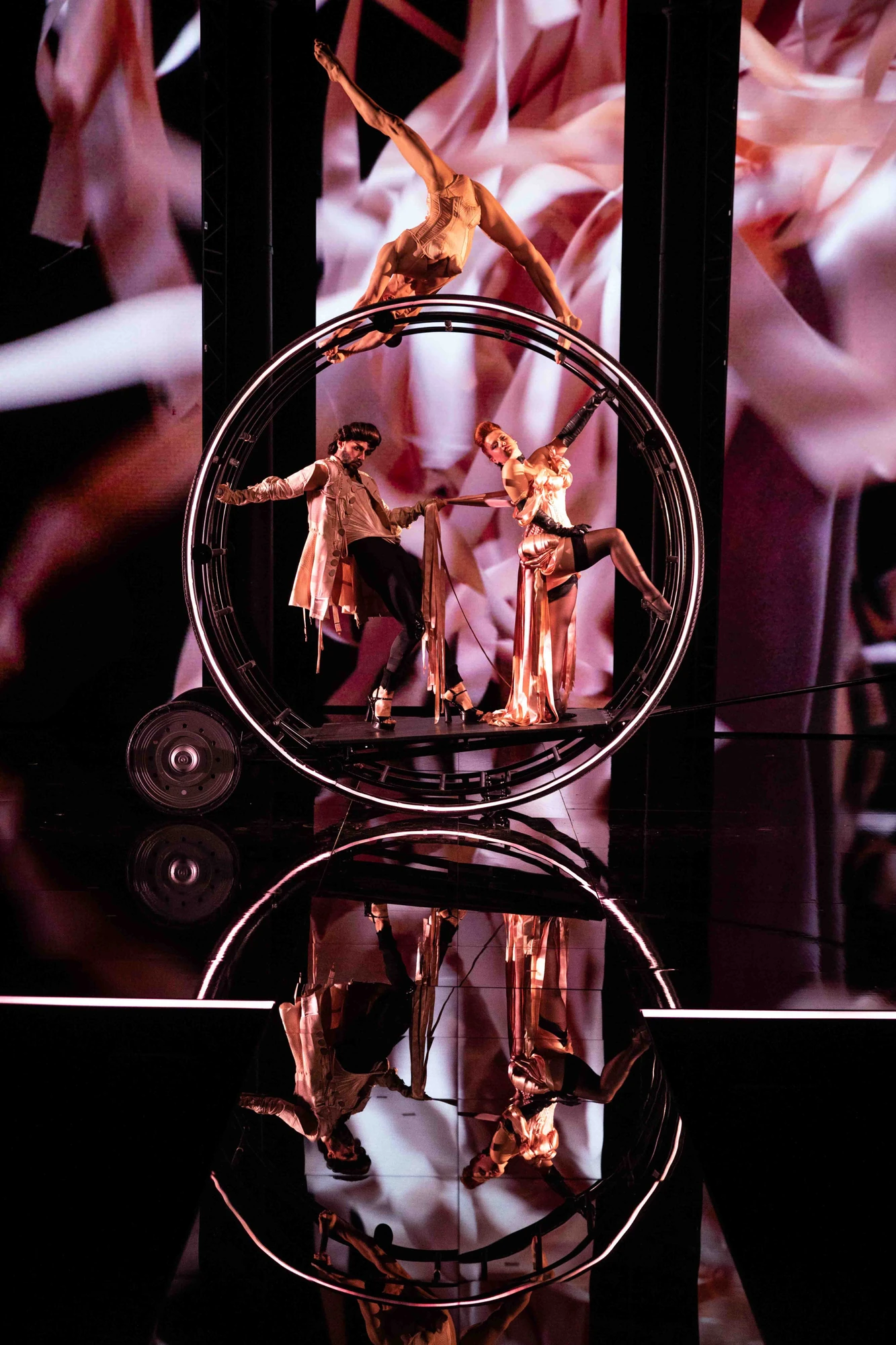 Jean Paul Gaultier Fashion Freak Show - elegantes Paar in einem Rad, Frau auf dem rollendem Rad macht Akrobatik