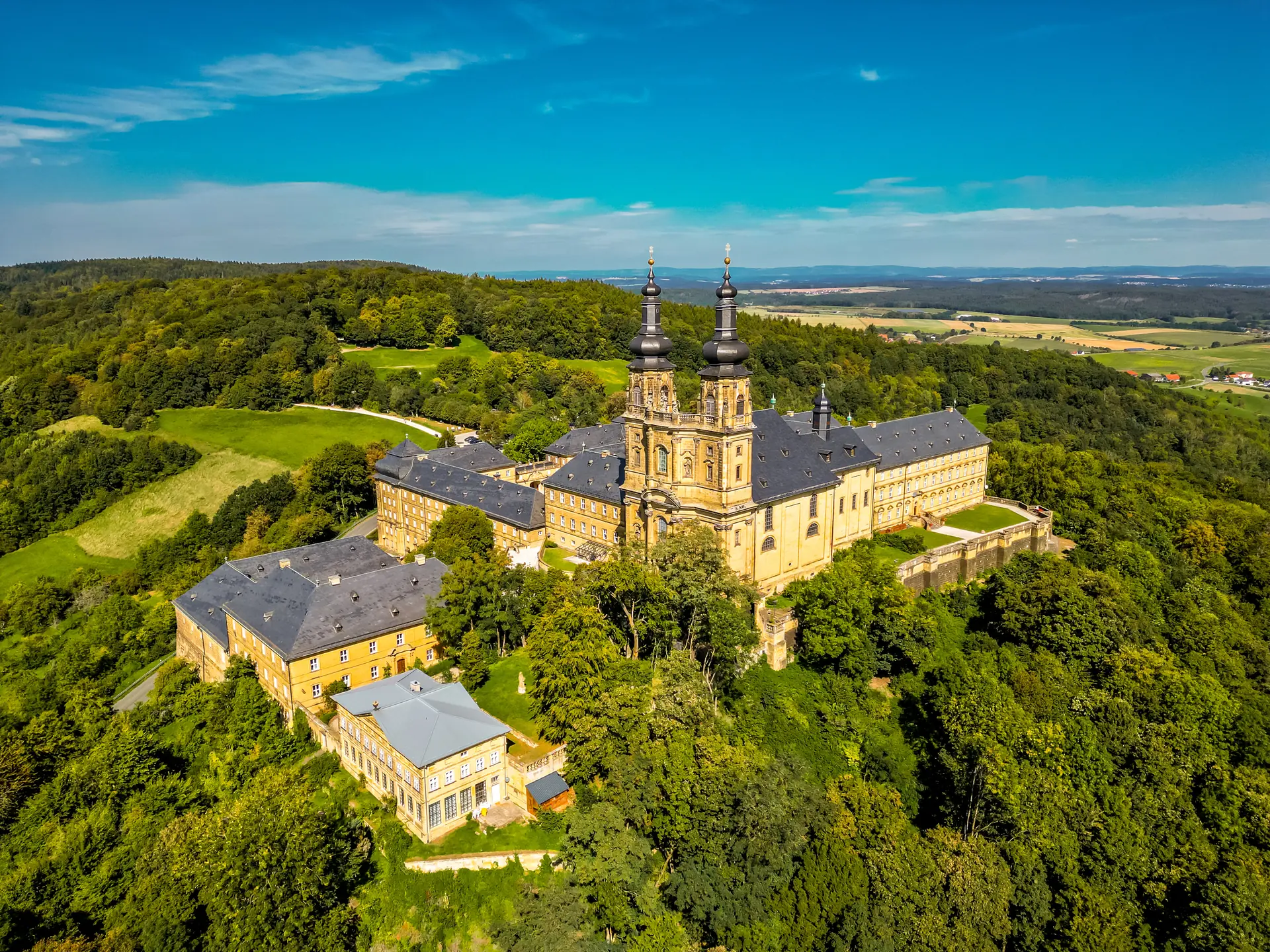 Kloster Banz aus der Vogelperspektive bei Sonnenschein umgeben von grünen Bäumen bei Bad Staffelstein