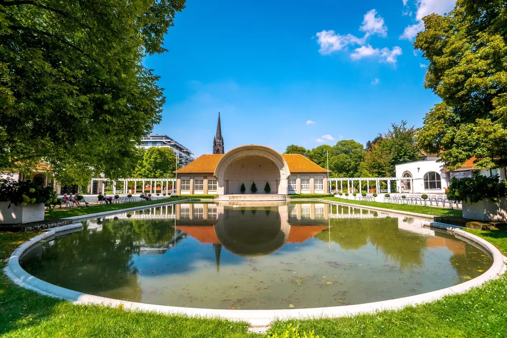 Panoramablick in den Kurpark von Bad Nauheim an einem sonnigen Tag mit einem Teich und Blick auf das Kurhaus